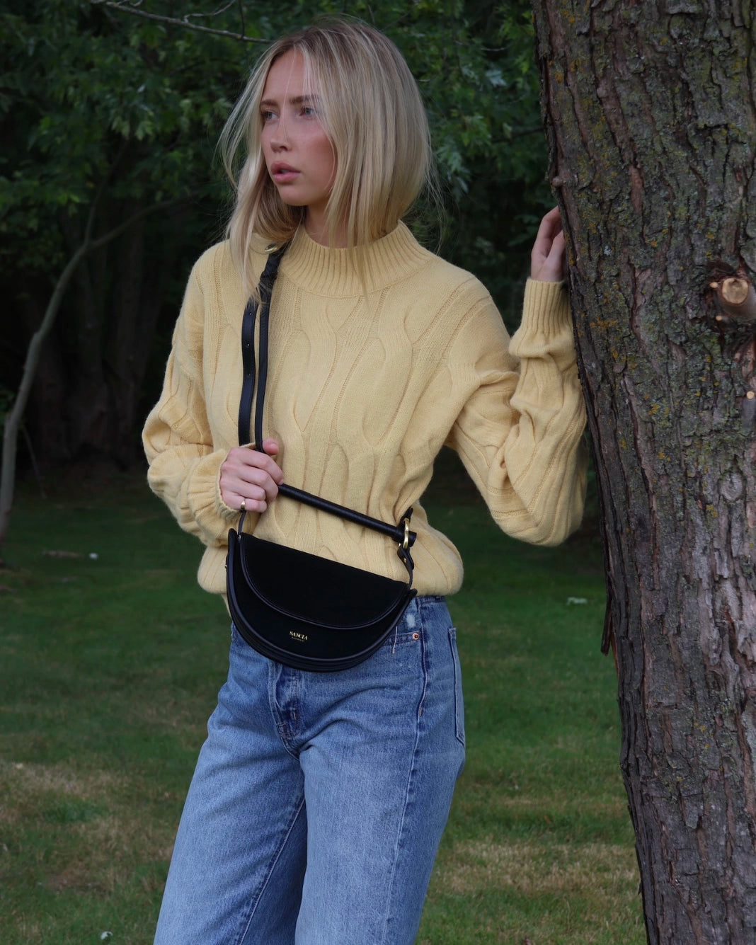 Woman in a yellow cable knit sweater standing next to a tree