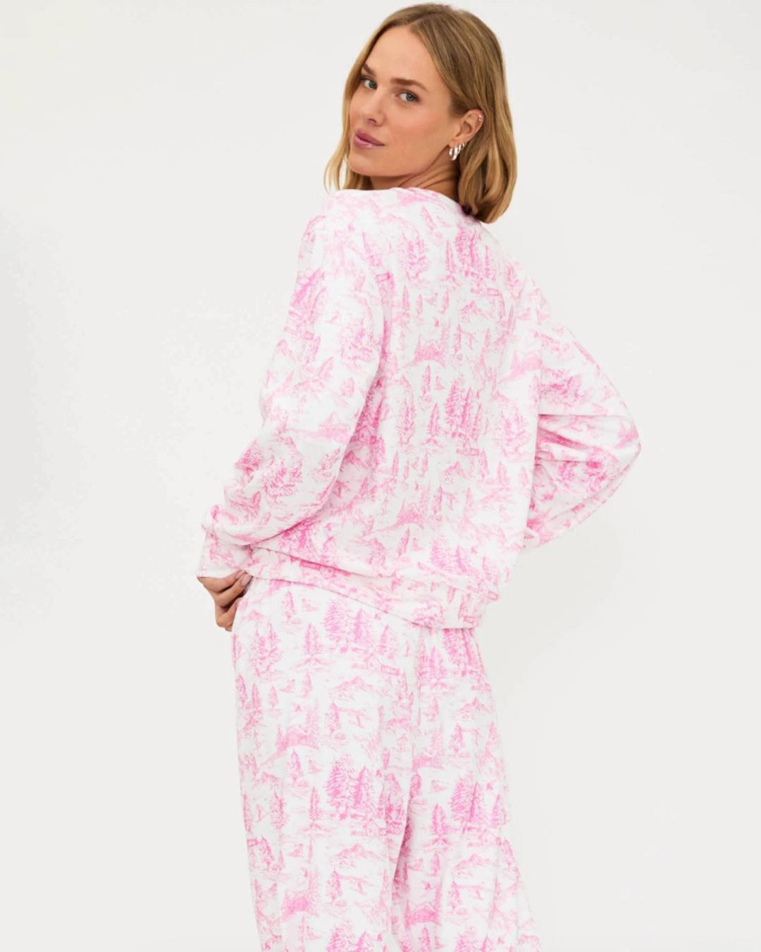 a woman wears a sweatshirt in white with pink toile ski pattern with the words 'SKI' on it