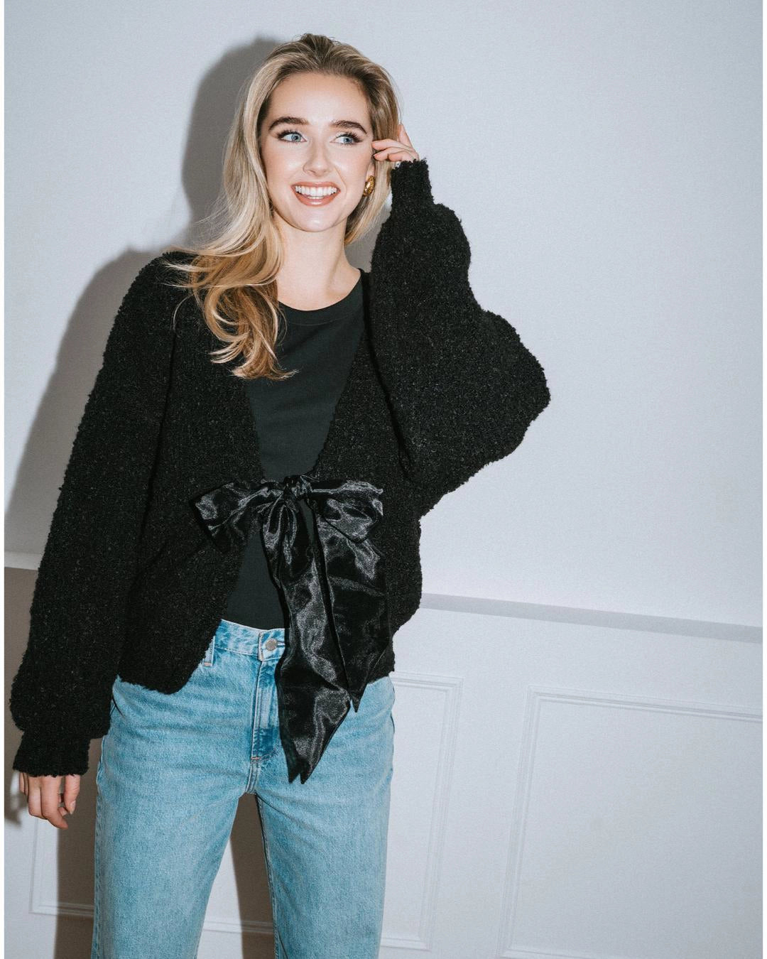 Woman wearing a black cardigan over a black turtleneck with a large black satin bow