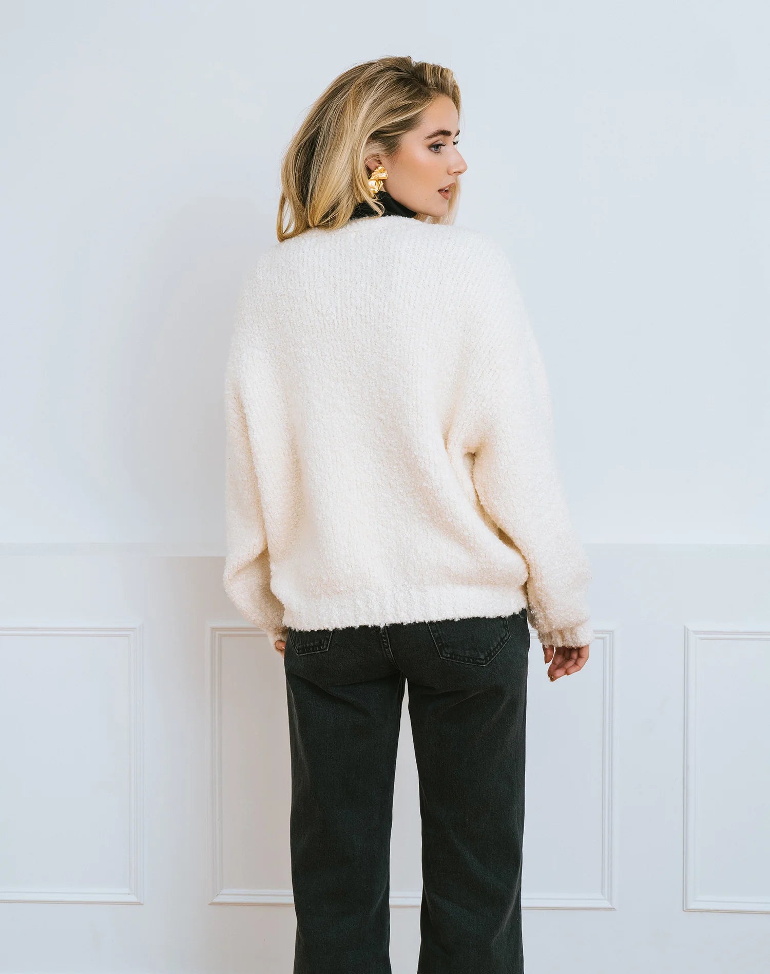 Woman wearing a cream cardigan over a black turtleneck with a large black satin bow