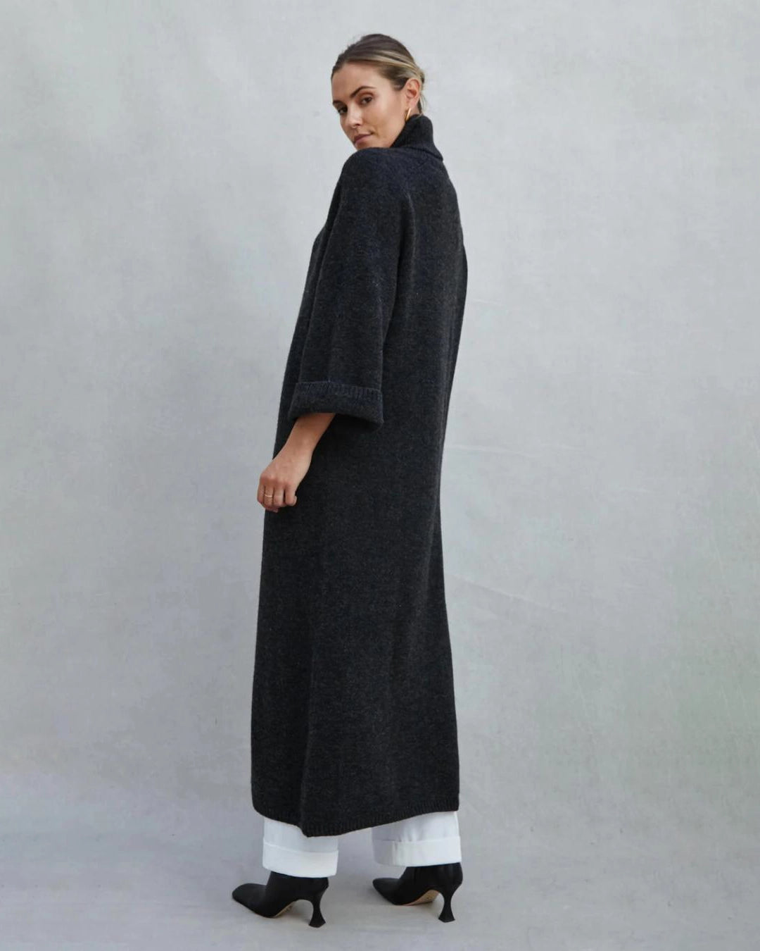 Woman wearing a long turtleneck sweater dress in black with a large slit up the front