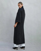 Woman wearing a long turtleneck sweater dress in black with a large slit up the front