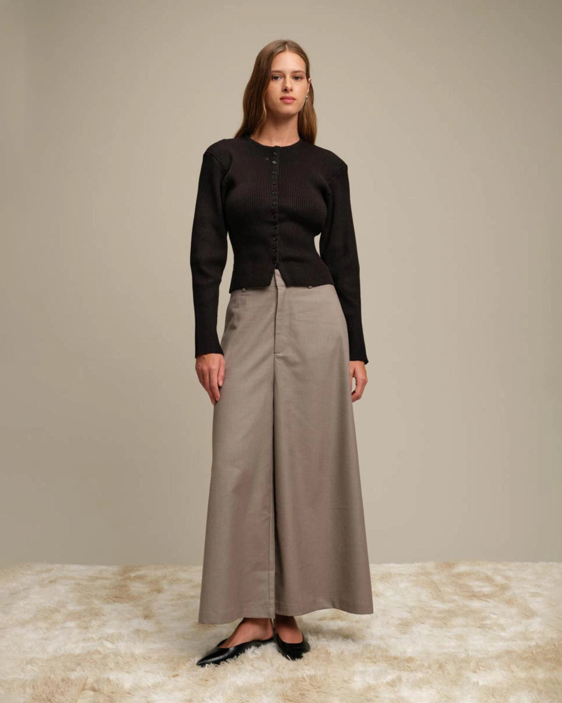 Woman wearing a black ribbed button down cardigan and beige wide-leg pants