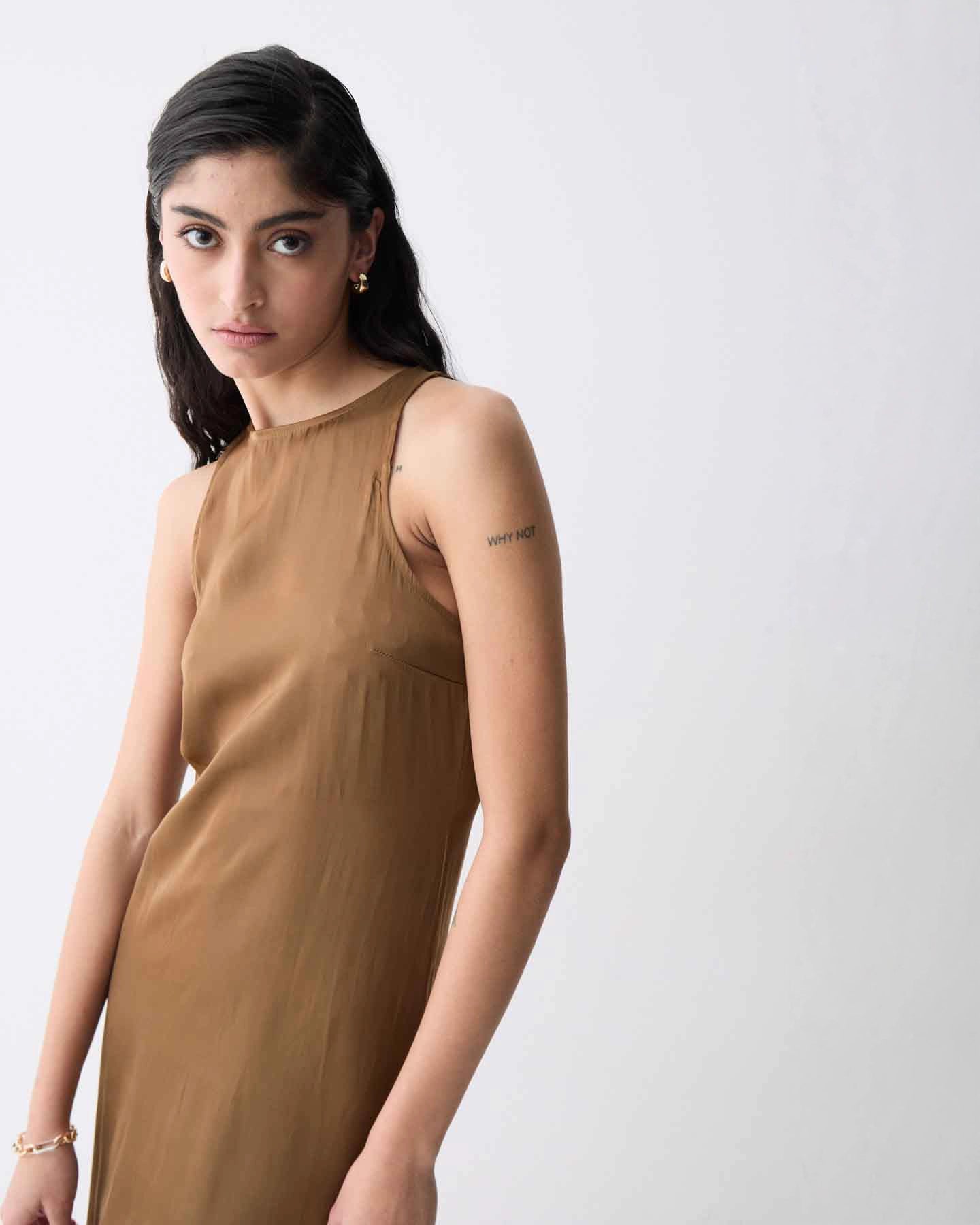 A woman wearing a sleeveless, midi length khaki dress with a round neckline.