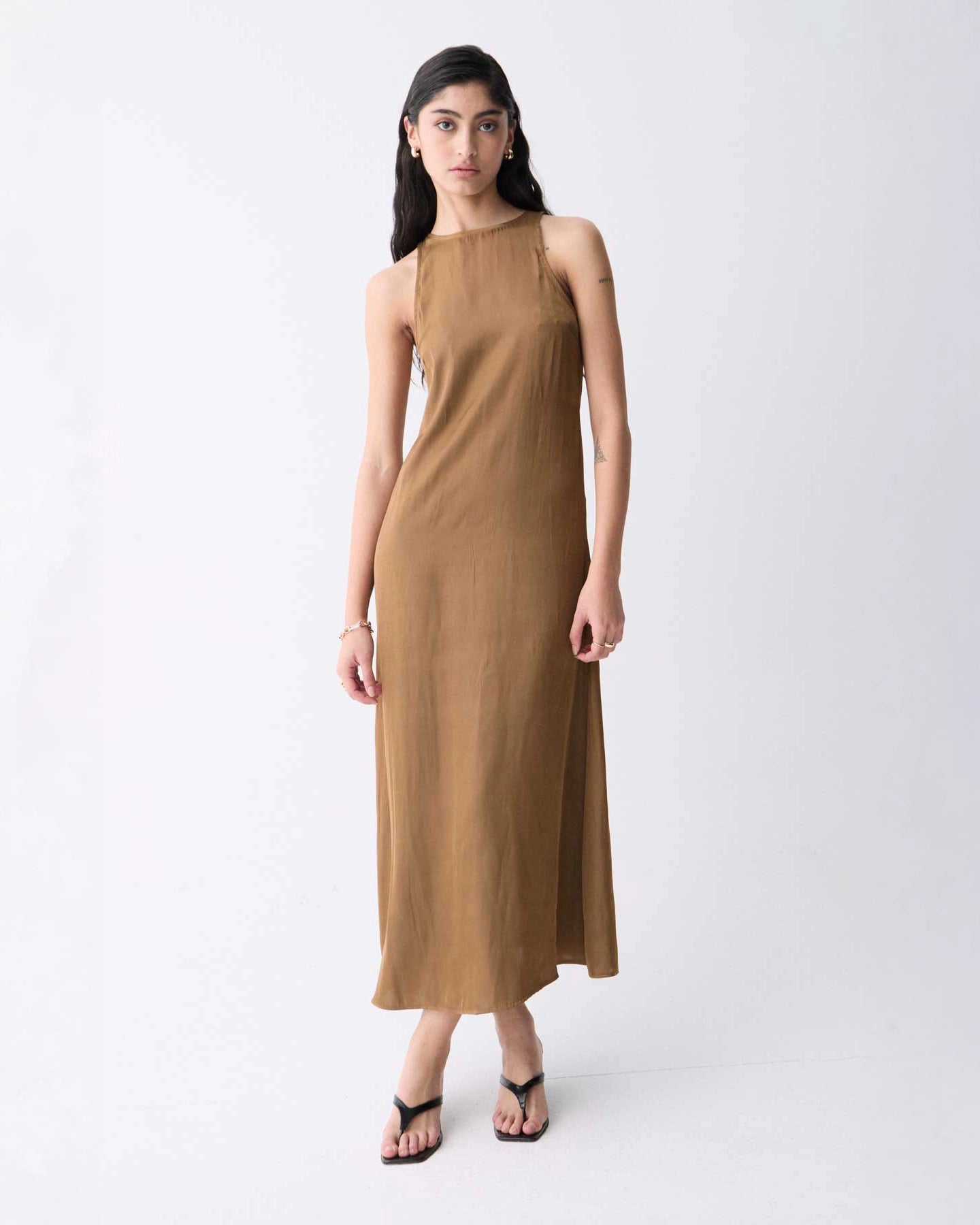 A woman wearing a sleeveless, midi length khaki dress with a round neckline.