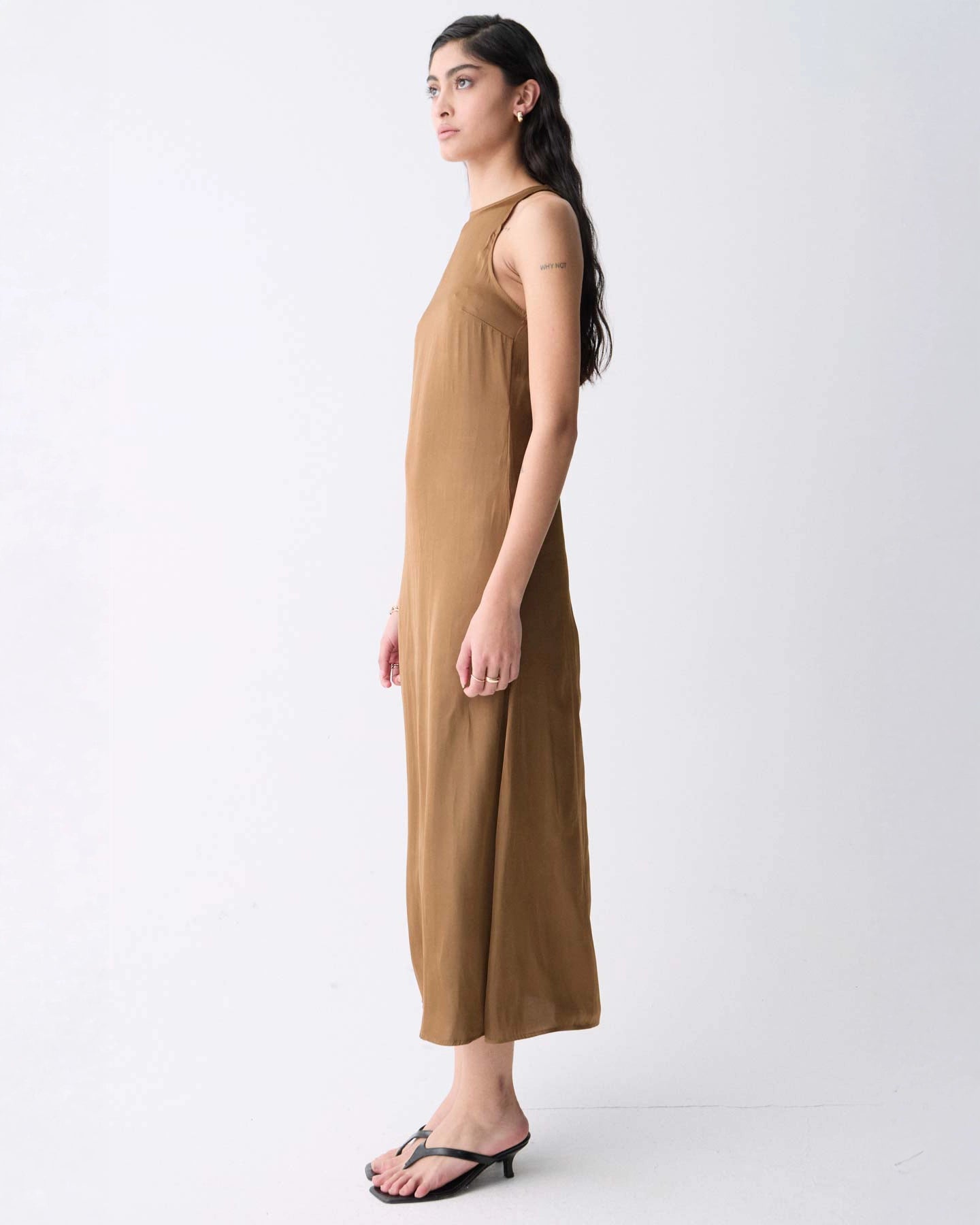 A woman wearing a sleeveless, midi length khaki dress with a round neckline.