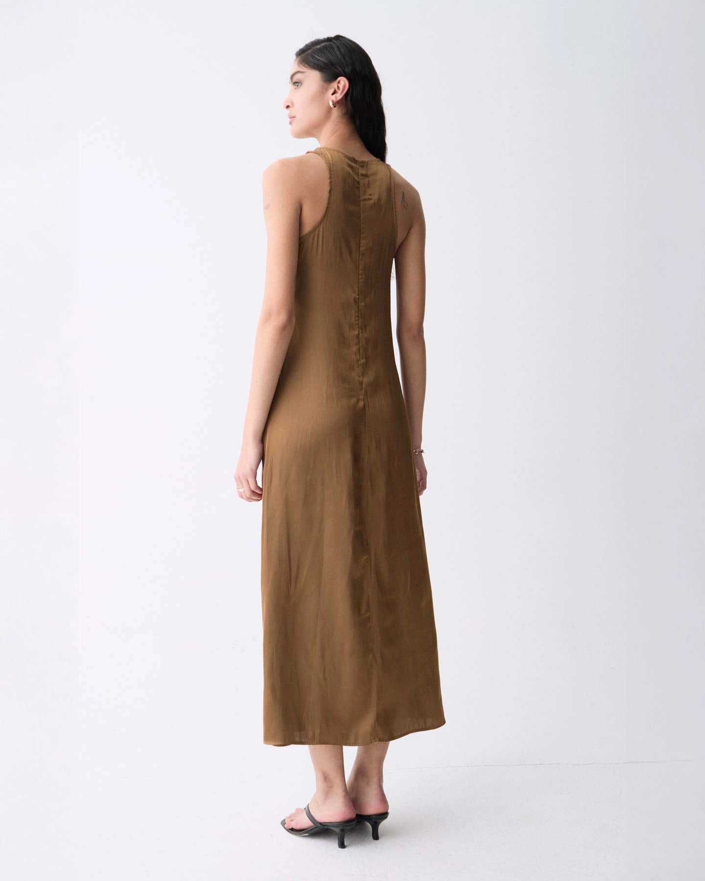 A woman wearing a sleeveless, midi length khaki dress with a round neckline.