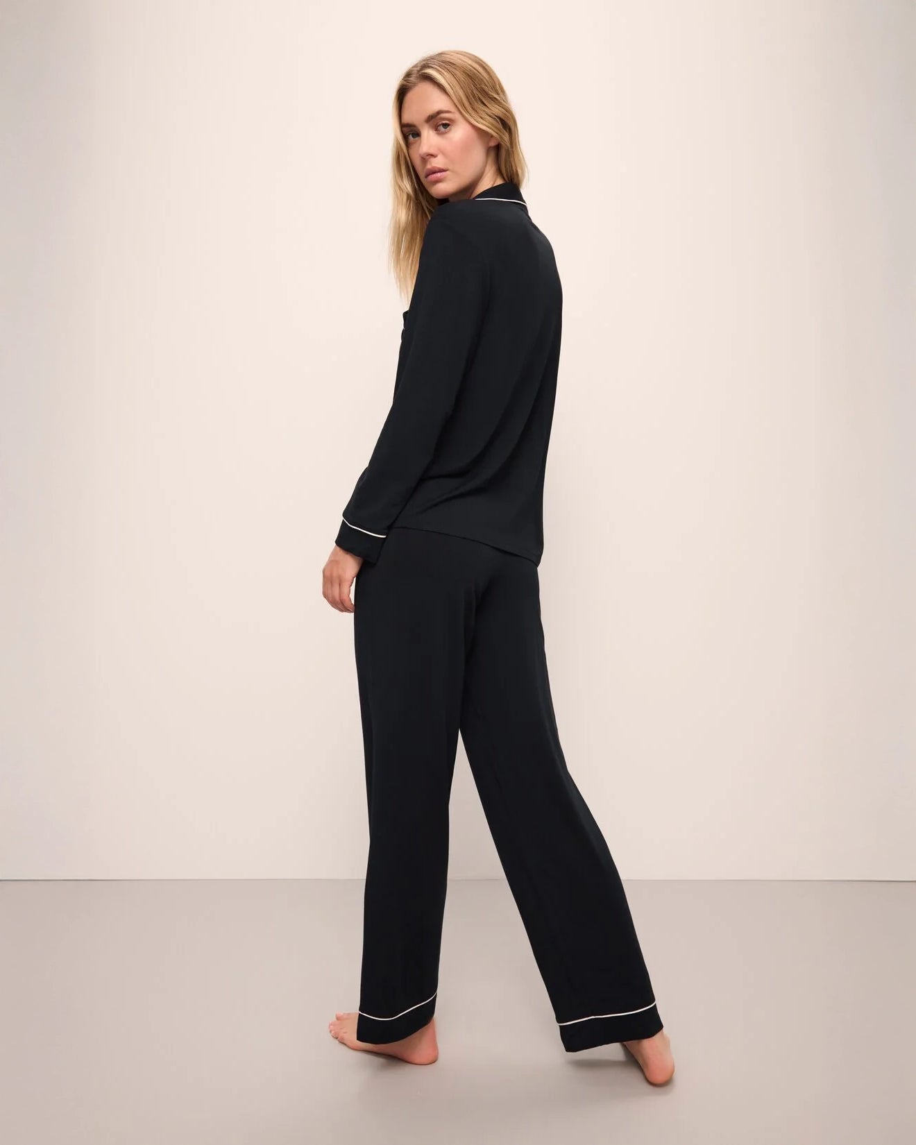 A woman wearing a black long pajama set with a button-up top and pants with light pink piping