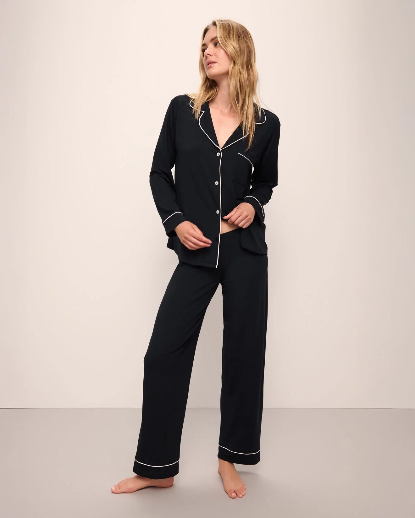 A woman wearing a black long pajama set with a button-up top and pants with light pink piping