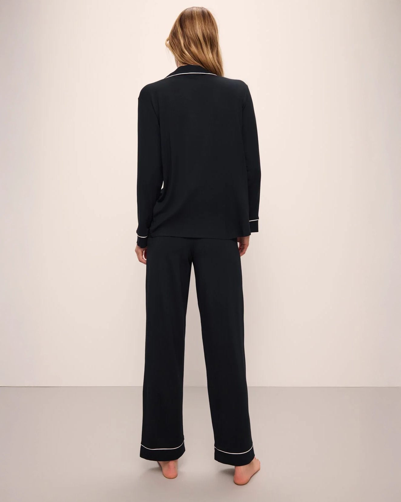 A woman wearing a black long pajama set with a button-up top and pants with light pink piping