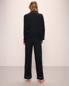 A woman wearing a black long pajama set with a button-up top and pants with light pink piping