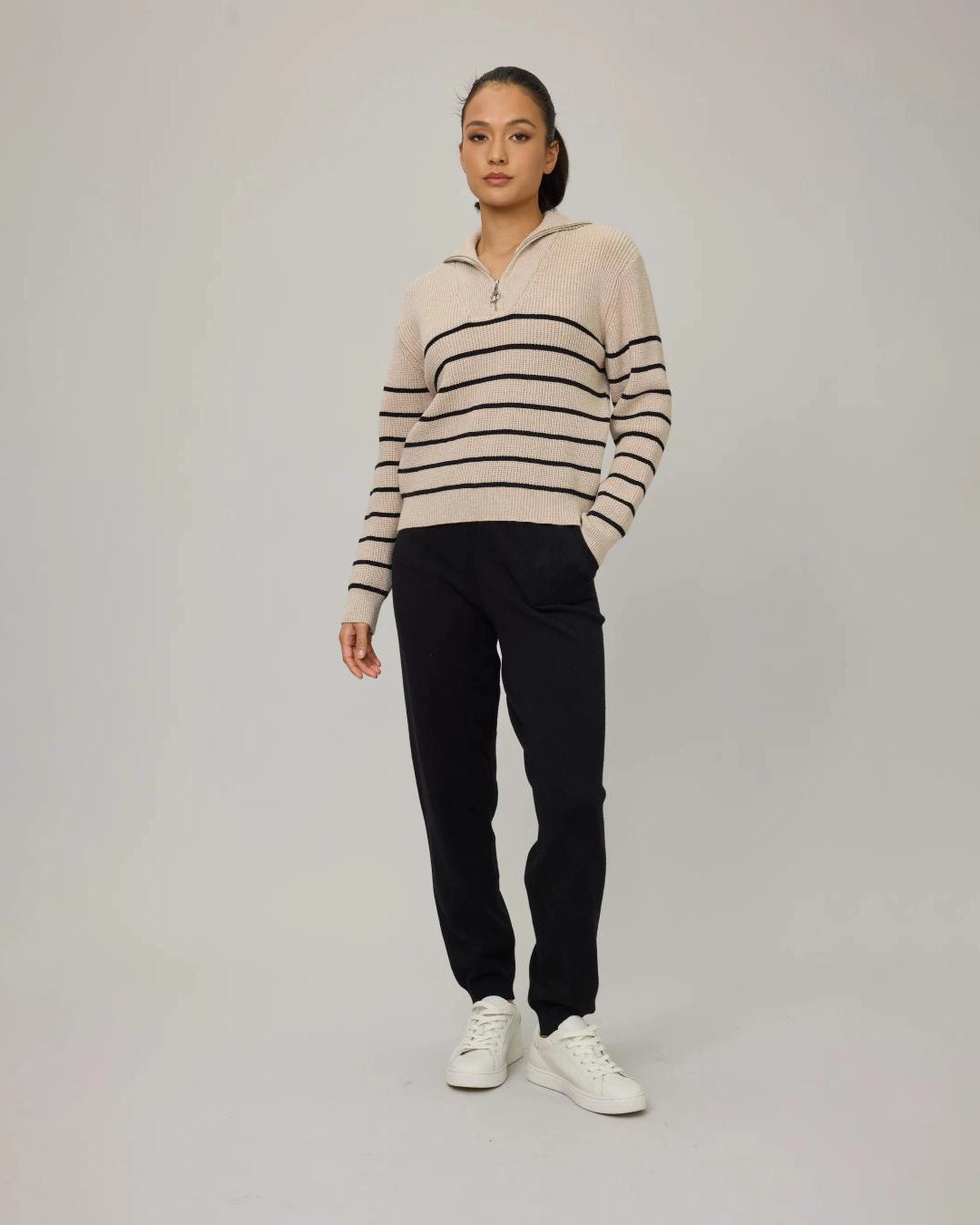 a woman wears a beige sweater with black stripes and a half zip