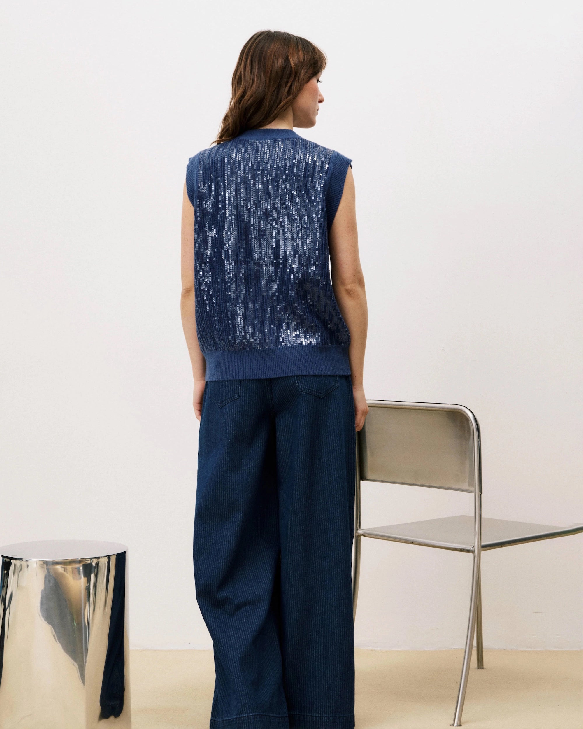 Woman wearing a blue sequin knit button down vest cardigan and wide blue pants