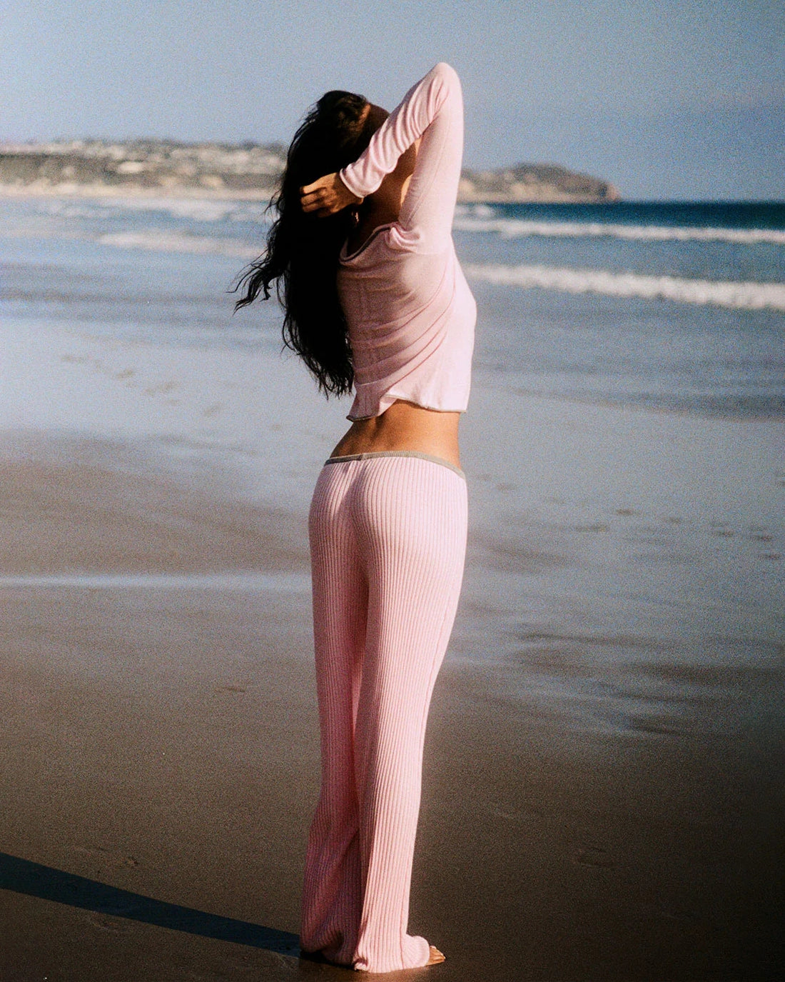 Person wearing a pink outfit standing on a beach with ocean waves