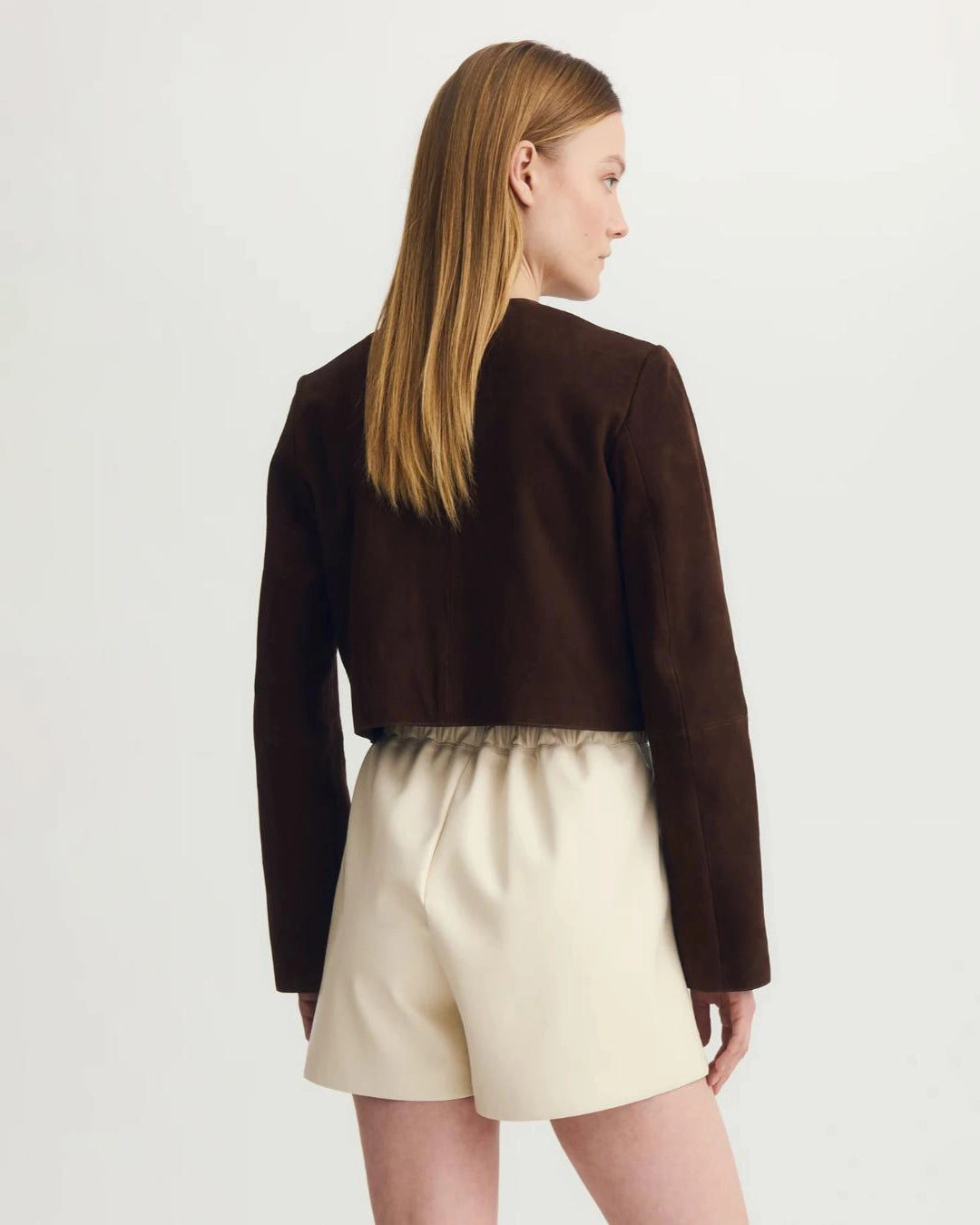 a woman wears a collarless brown suede jacket