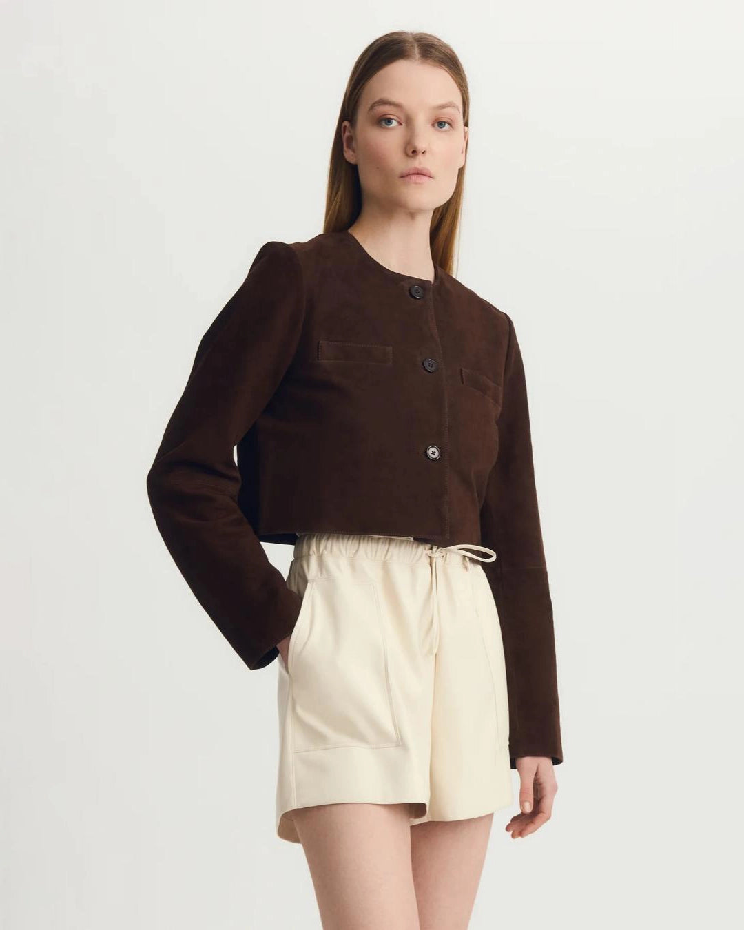 a woman wears a collarless brown suede jacket