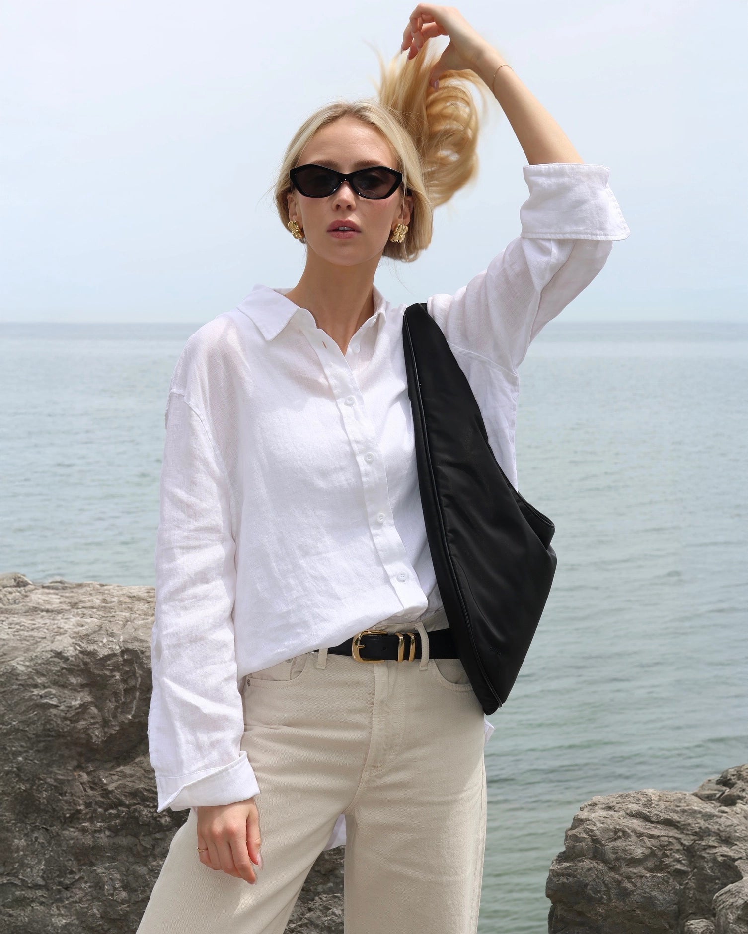 Woman in a white linen shirt and beige pants standing by the water