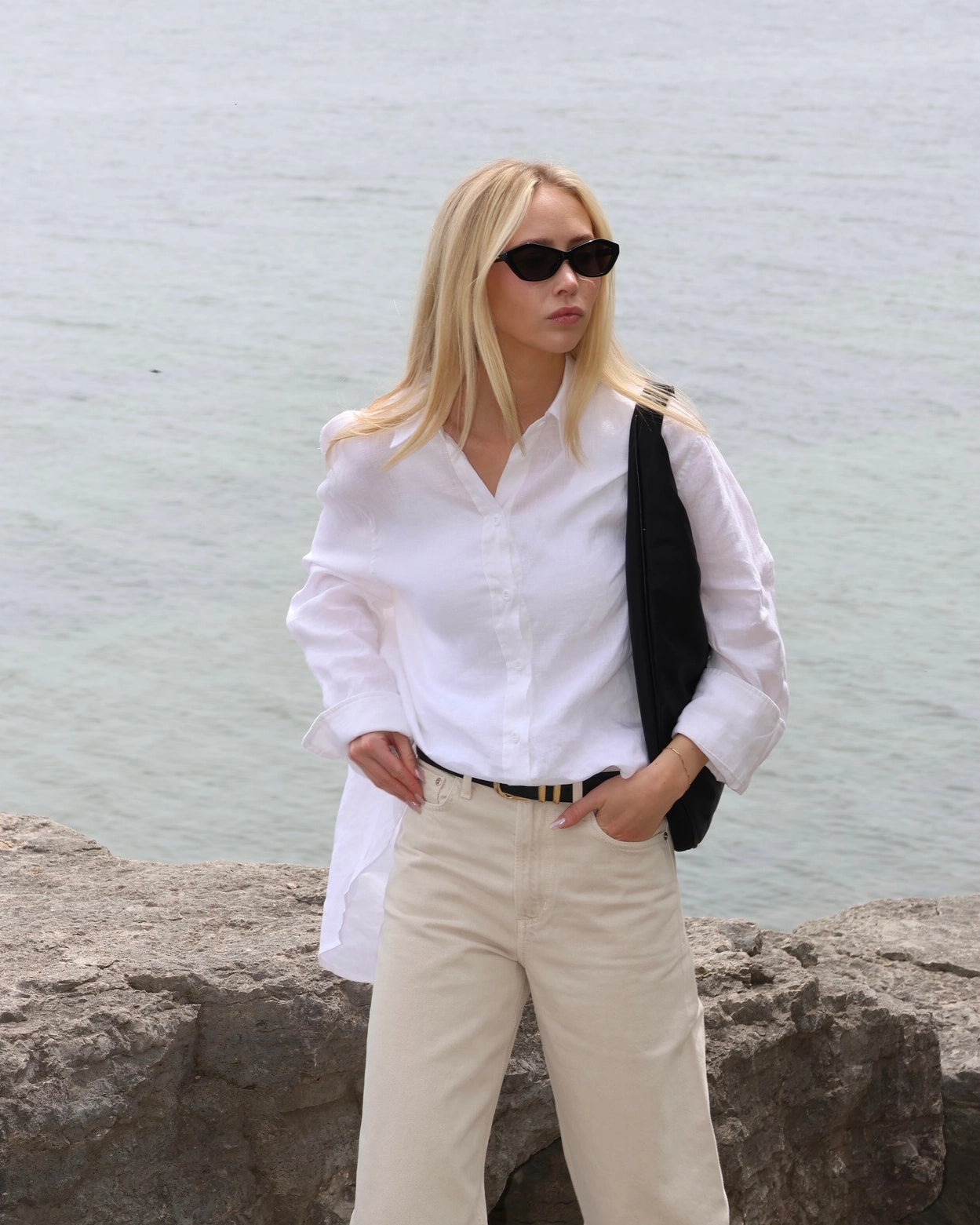 Woman in a white linen shirt and beige pants standing by the water
