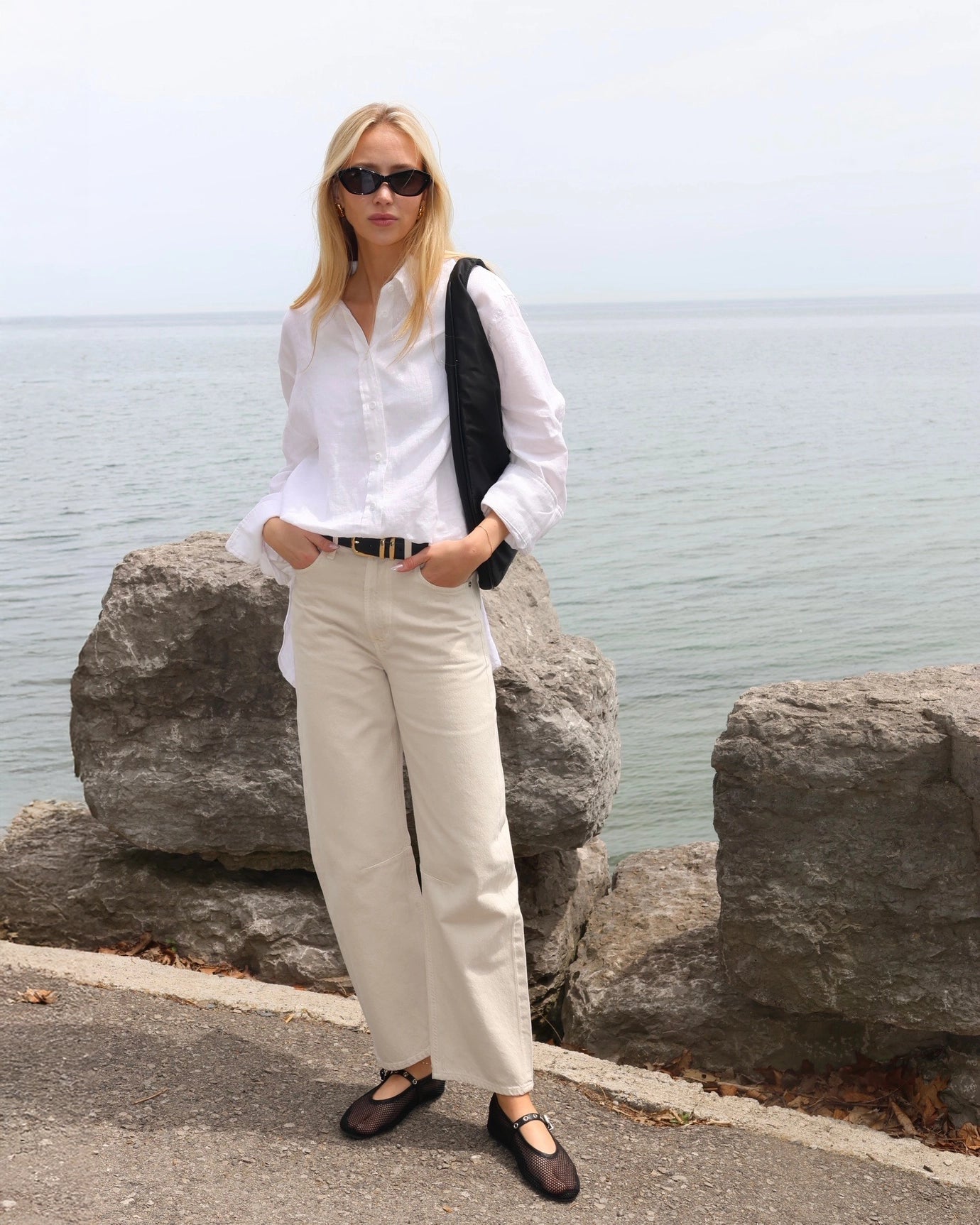 Woman in a white linen shirt and beige pants standing by the water