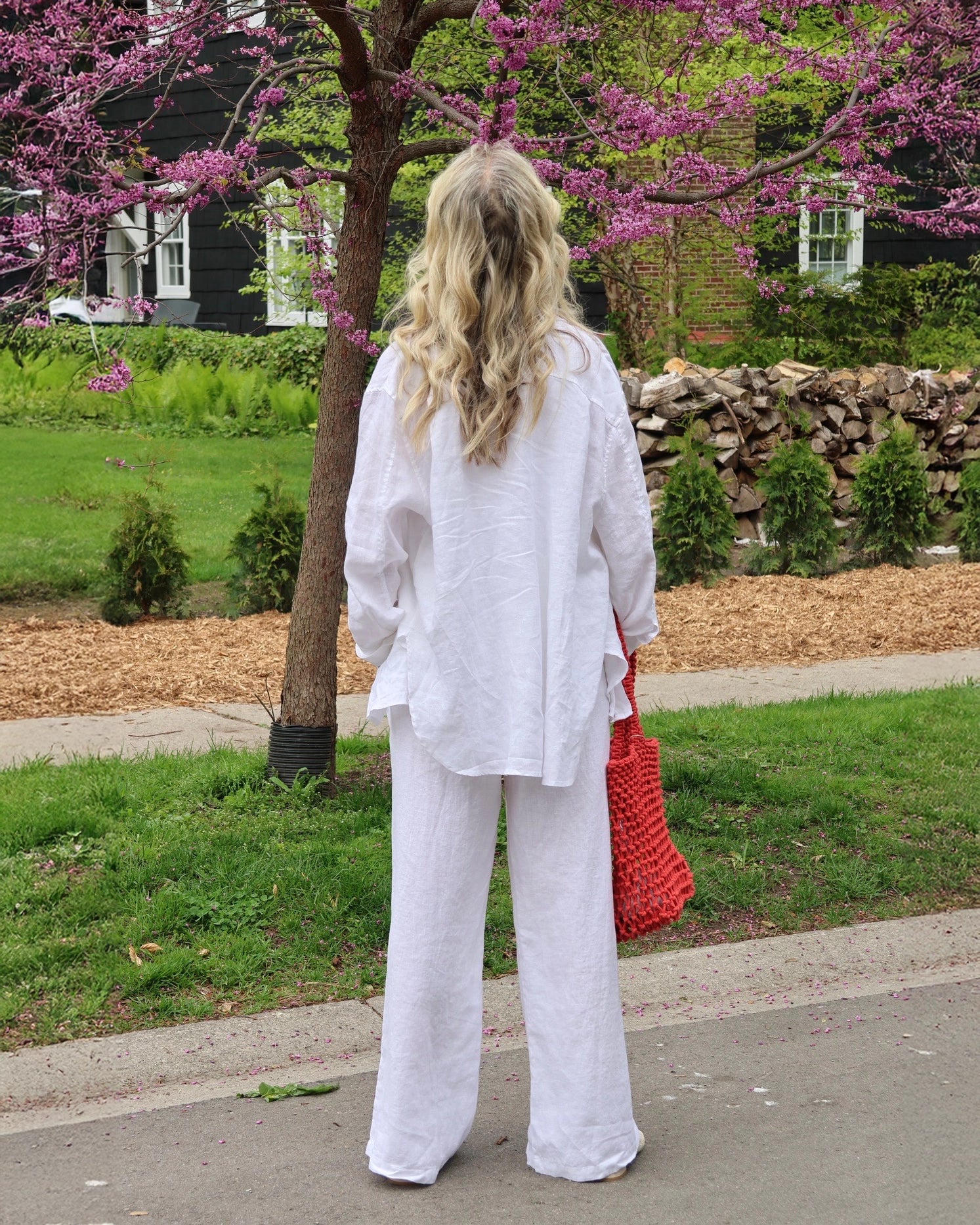 Woman in a white linen shirt and pants outdoors by cherry blossoms