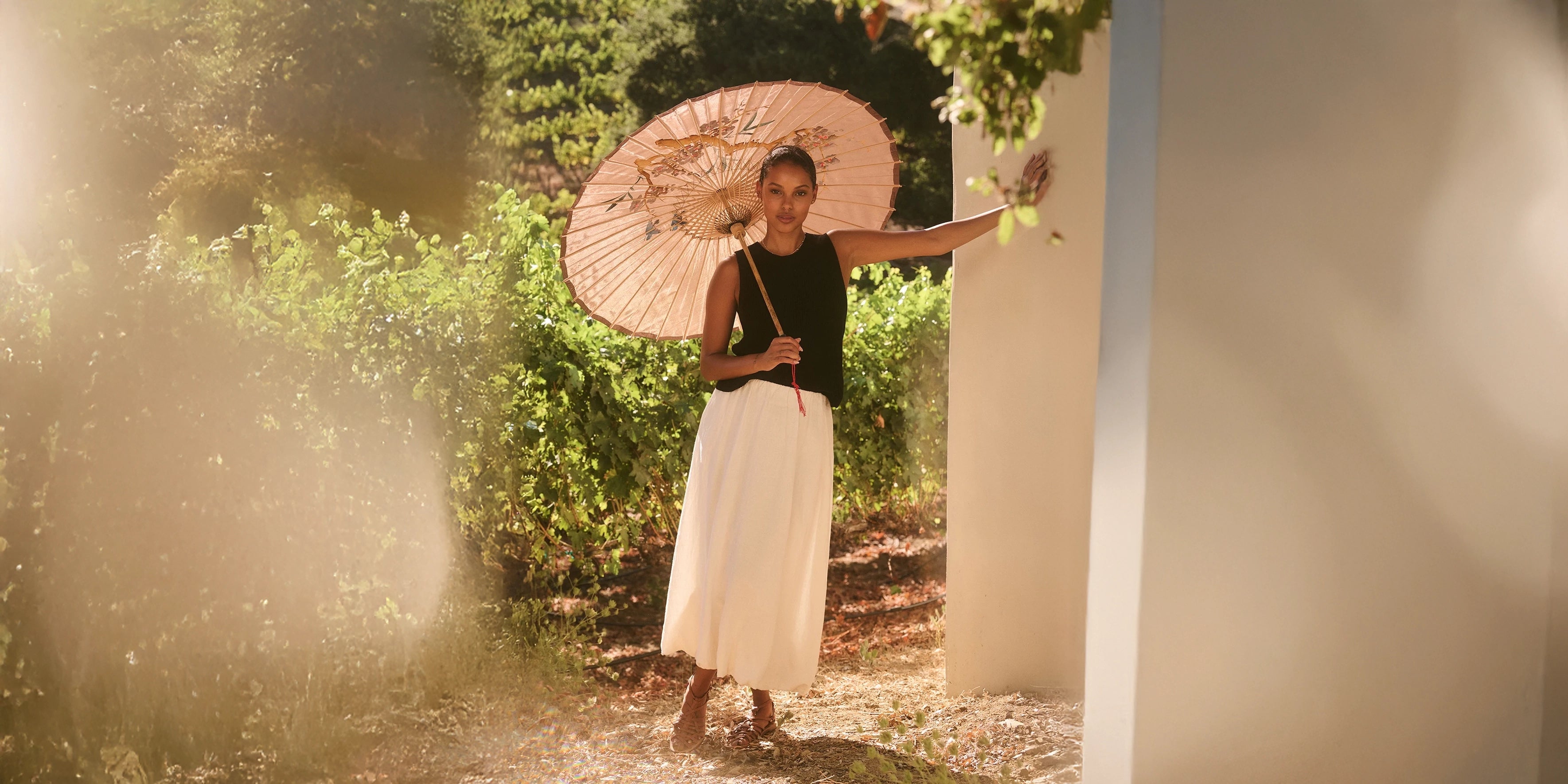 A woman wears a black sleeveless top and linen skirt with a parasol in the summer