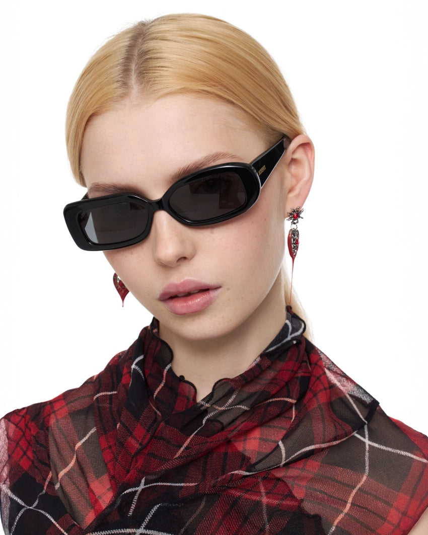 Woman wearing Jaquemus Rond Carre Sunglasses in Black with gold detail and plaid shirt