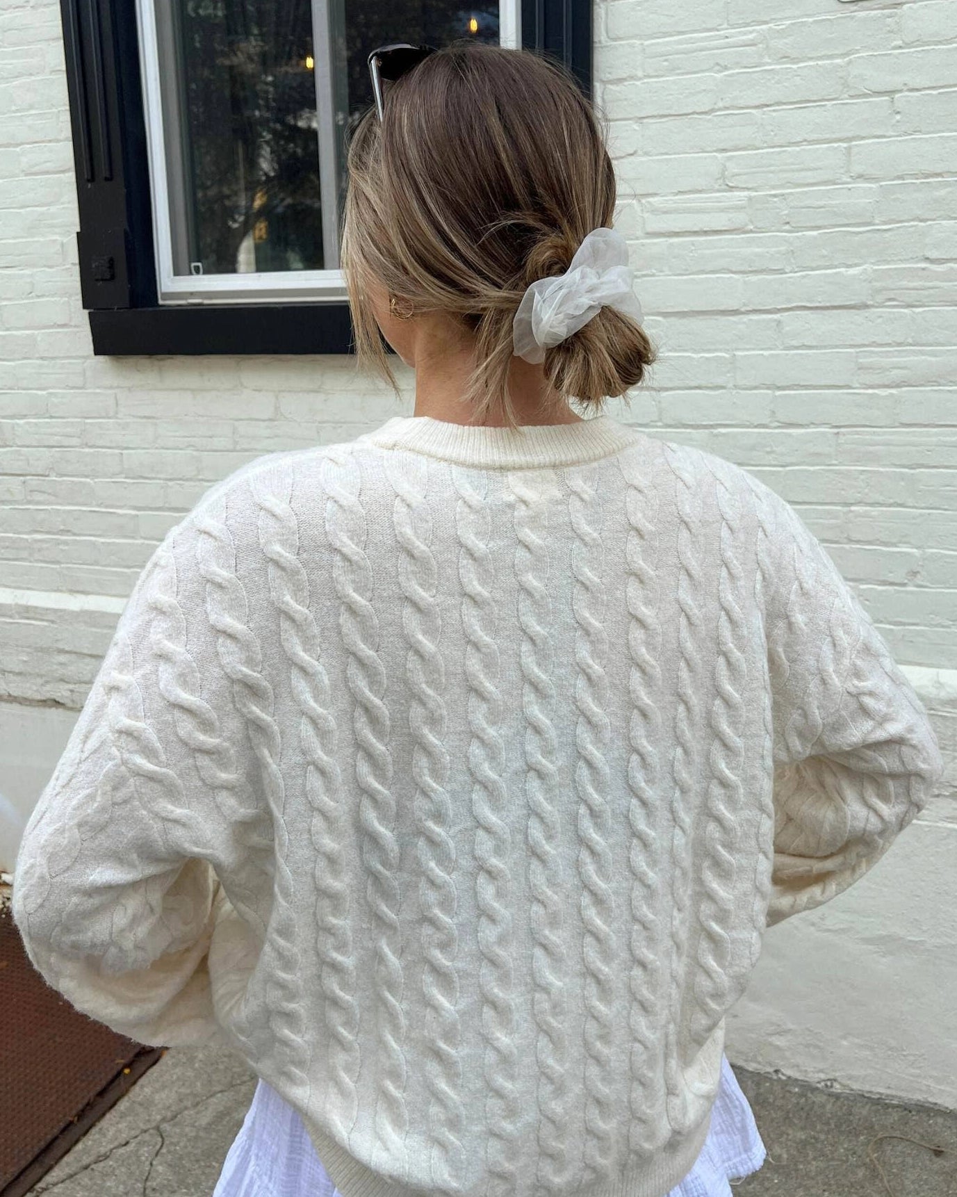 Person wearing a white chiffon scrunchie and cable knit sweater