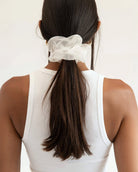 Person with long dark hair tied in a ponytail with a white chiffon scrunchie