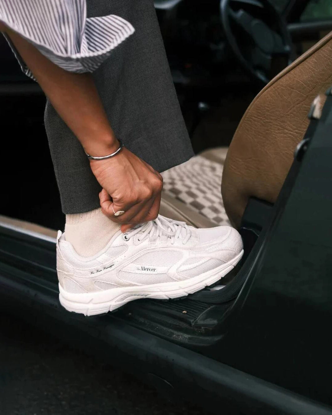 Person wearing a white sneaker stepping into a car.