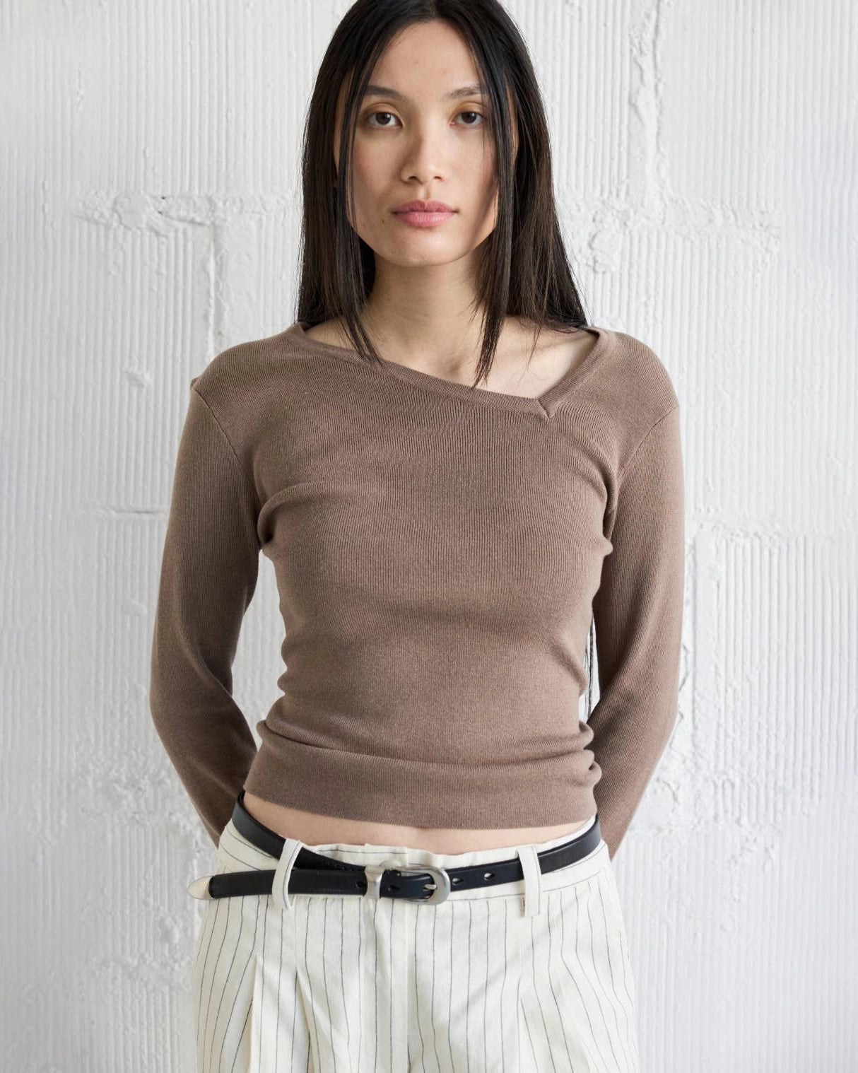 Woman wearing a brown knit sweater with asymmetrical neckline