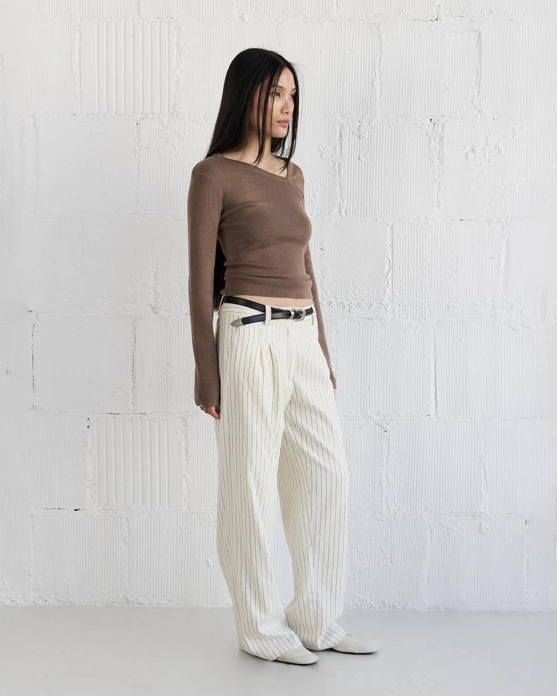 Woman wearing a brown knit sweater with asymmetrical neckline and white striped pants