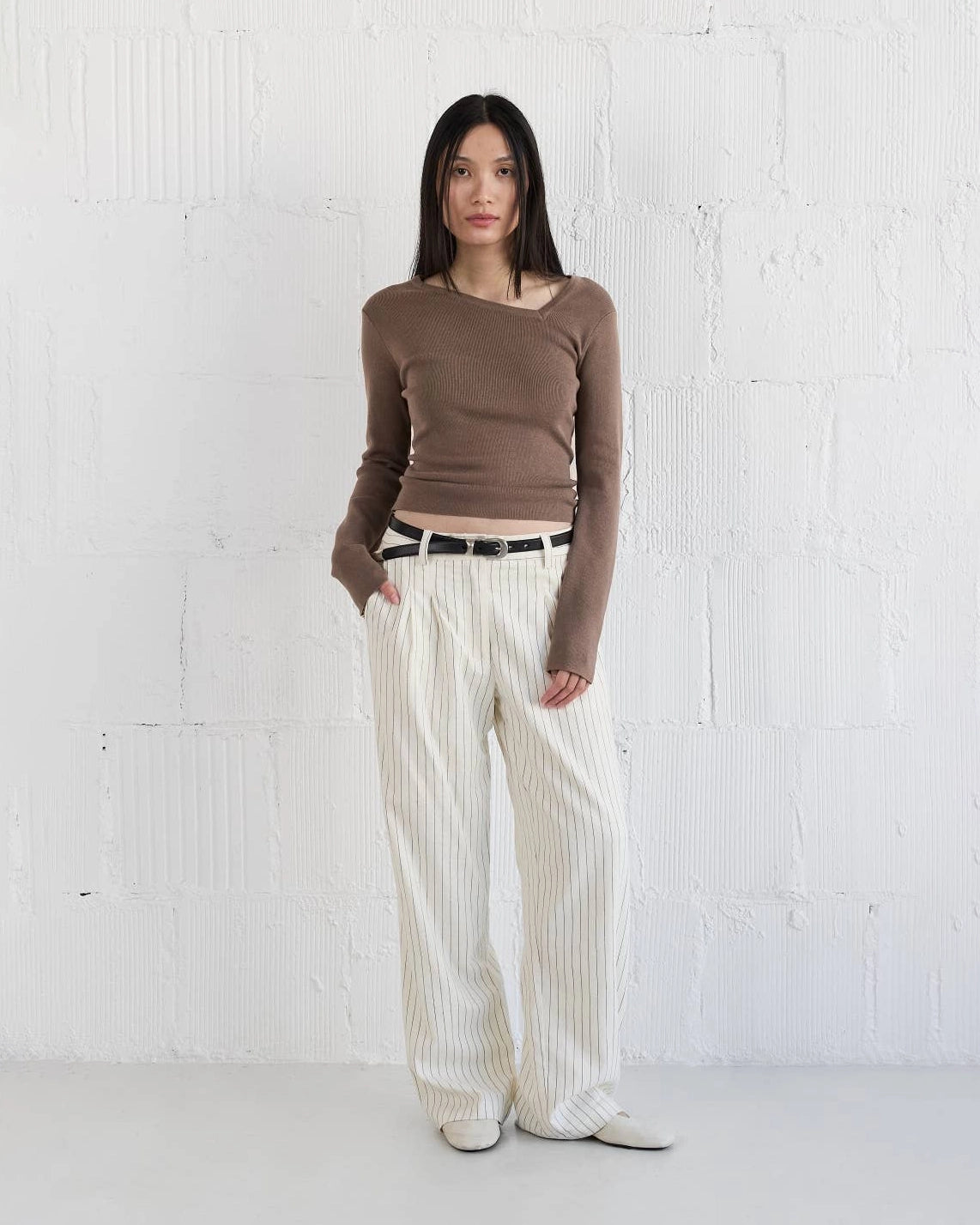 Woman wearing a brown knit sweater with asymmetrical neckline and white striped pants