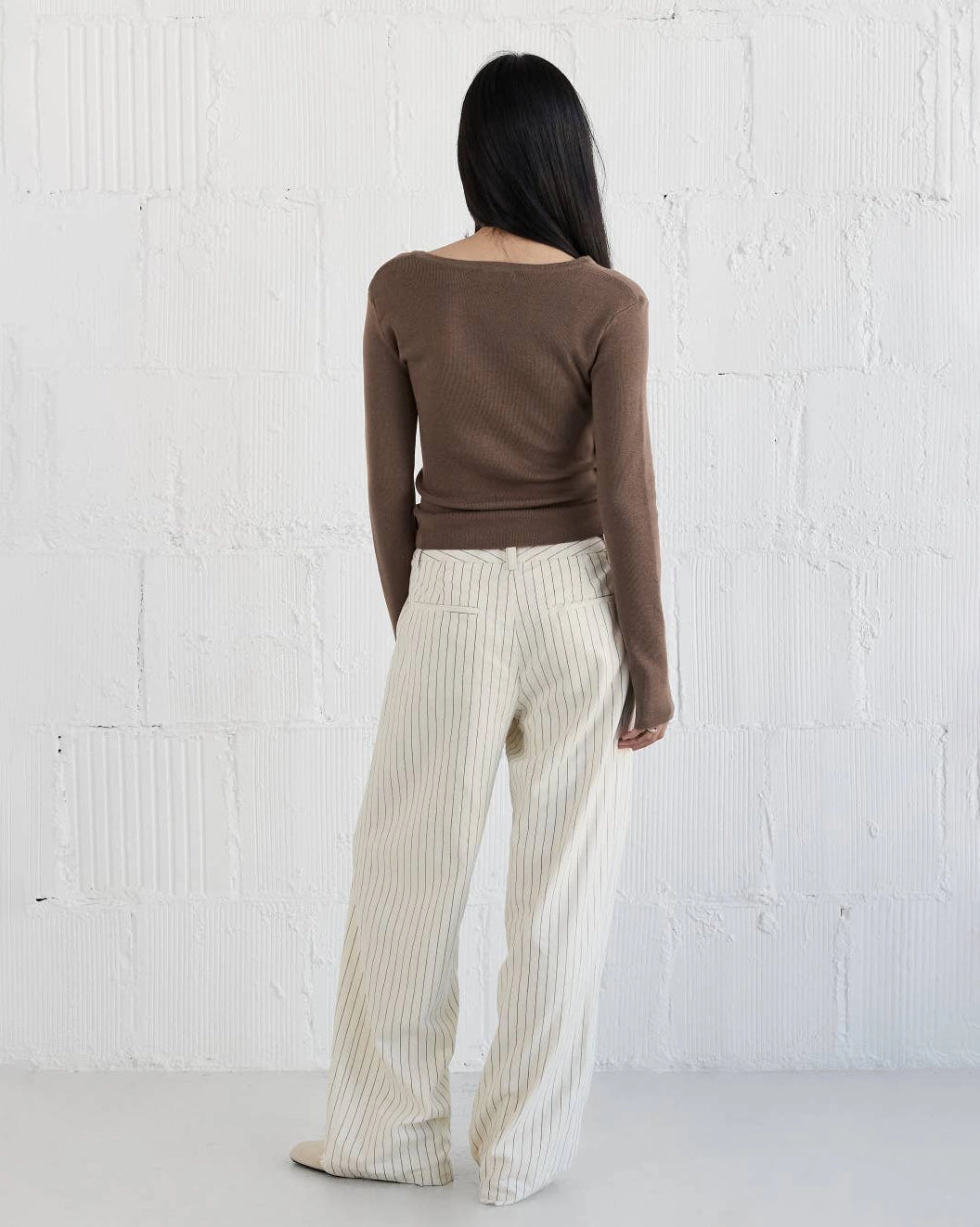 Woman wearing a brown knit sweater with asymmetrical neckline and white striped pants