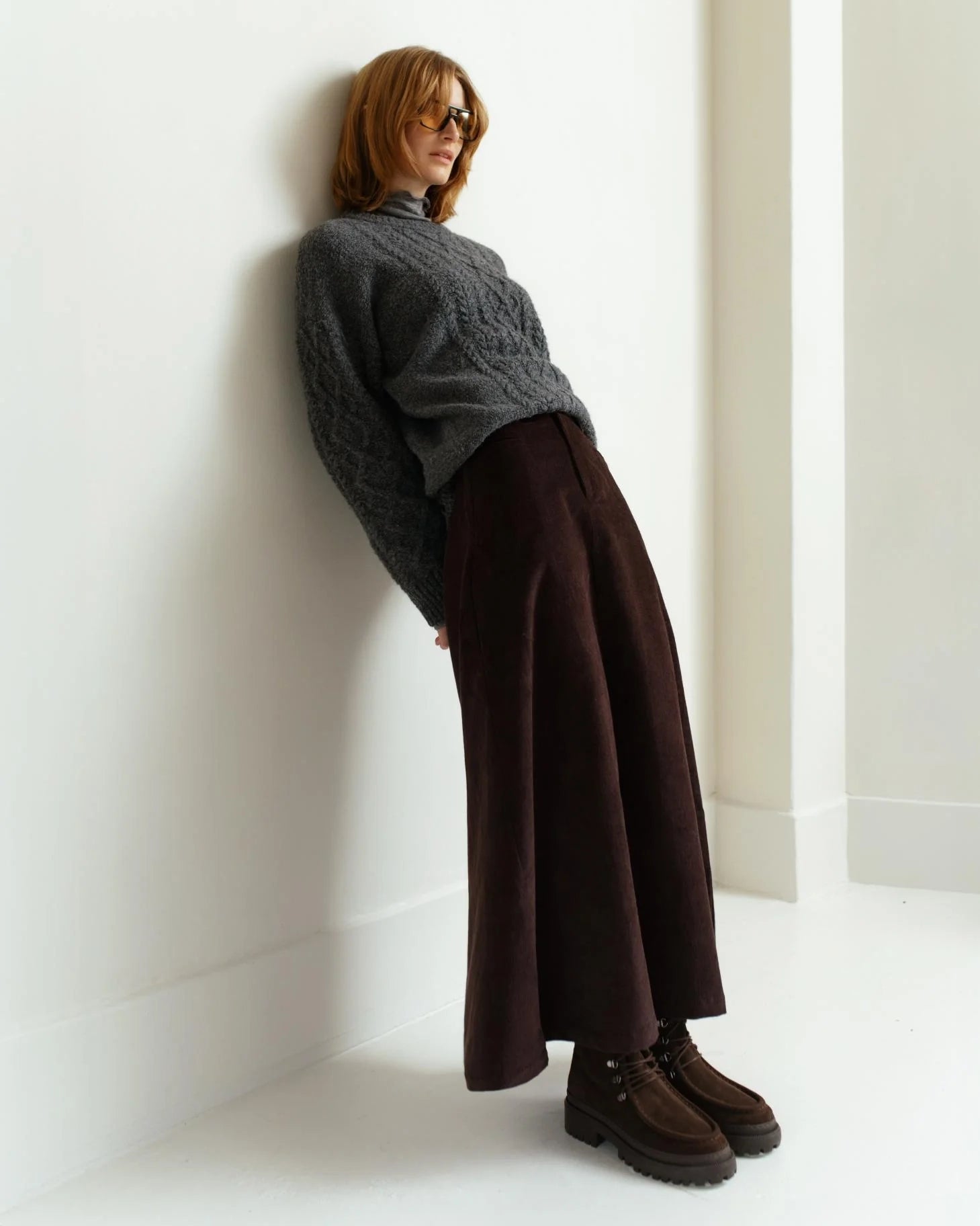 a woman wearing a gray cable knit sweater wiht brown skirt