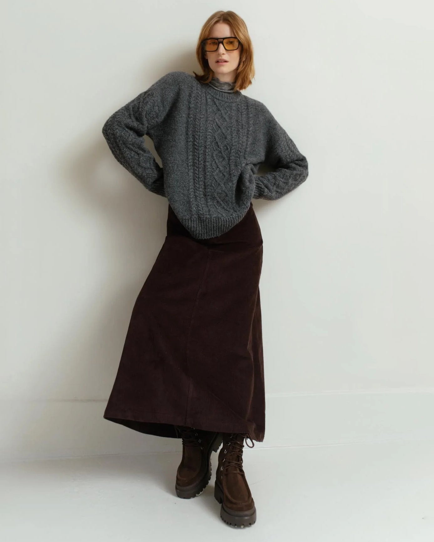 a woman wearing a gray cable knit sweater with brown skirt