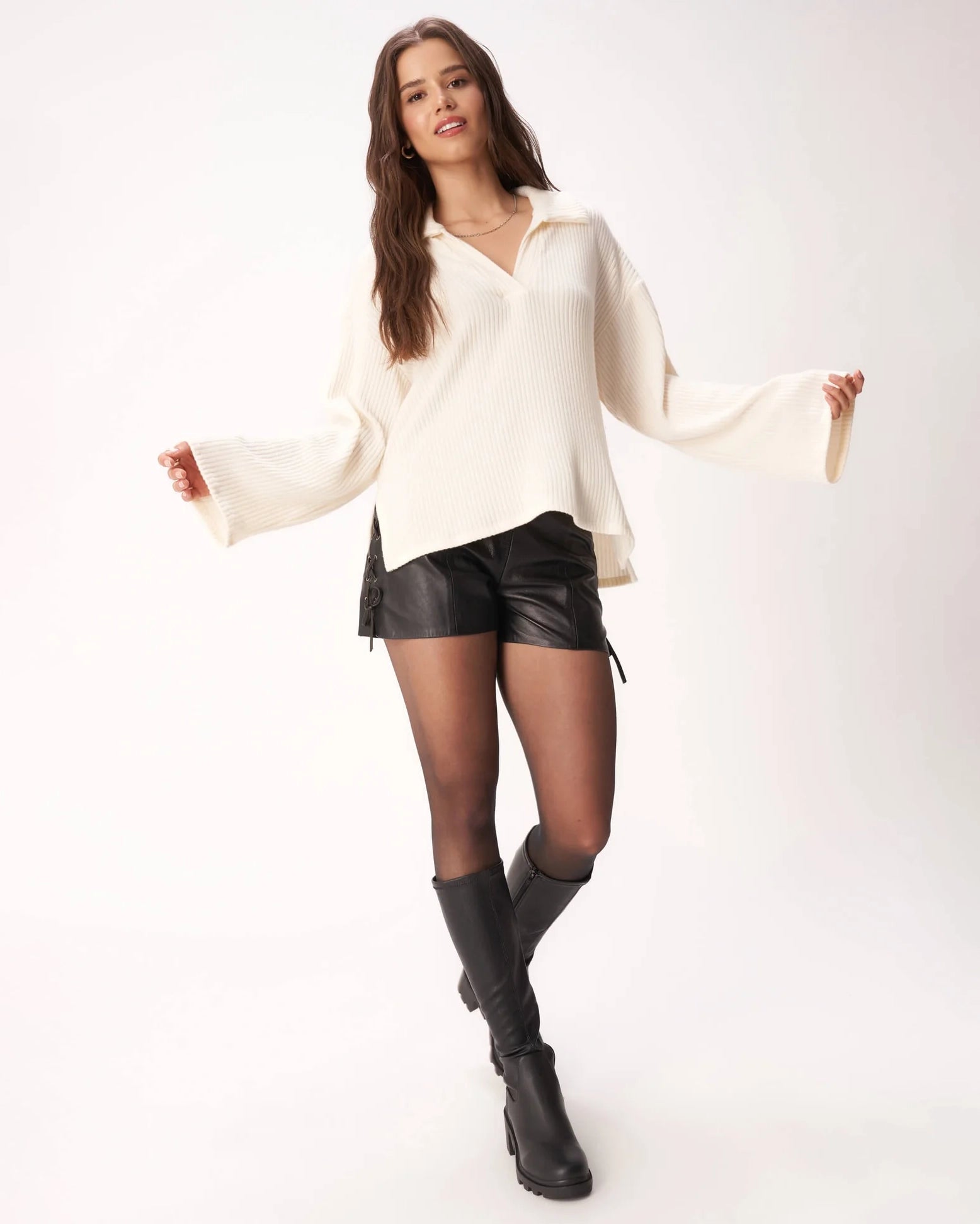 Woman wearing a ribbed cream v neck sweater and black leather shorts