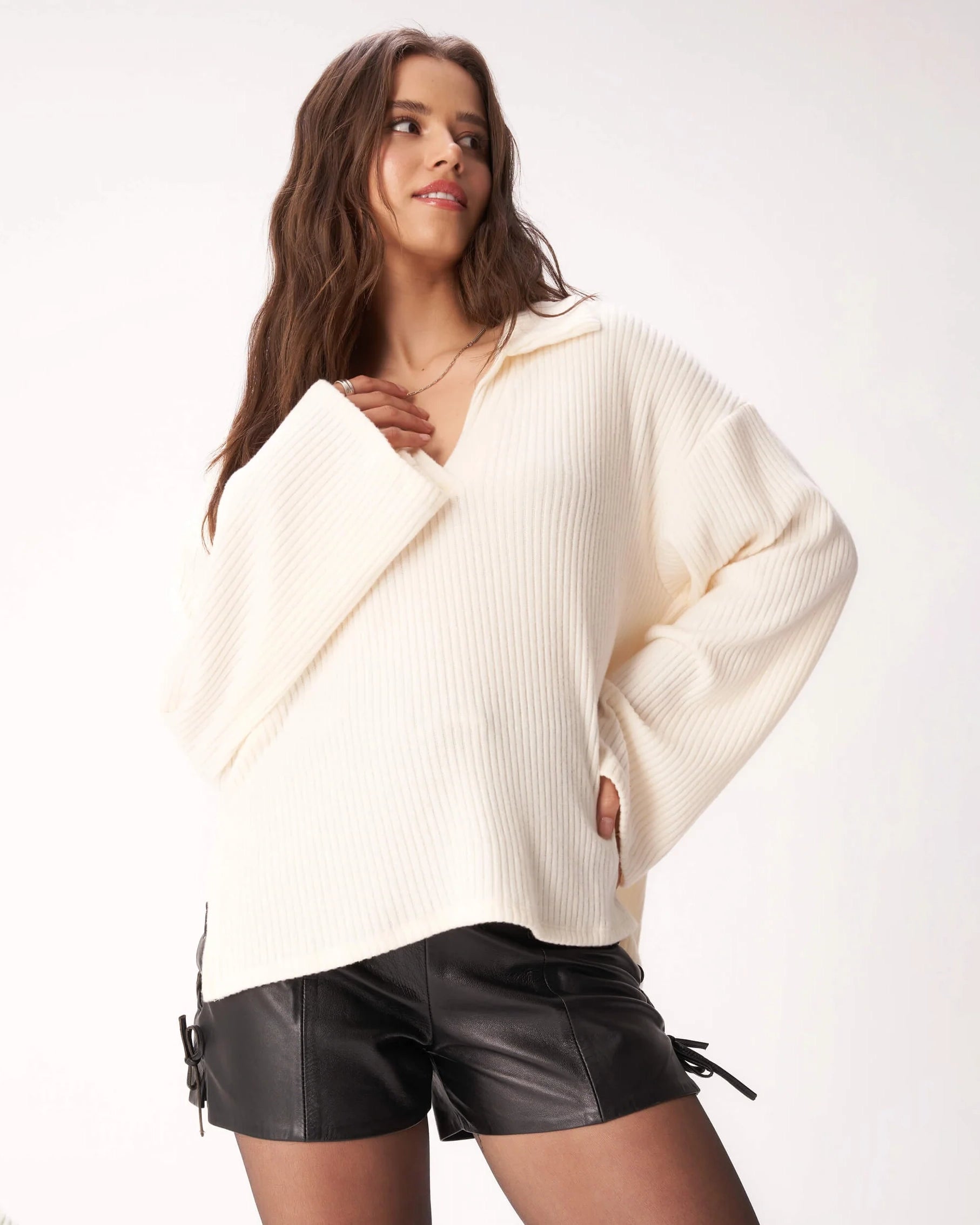 Woman wearing a ribbed cream v neck sweater and black leather shorts