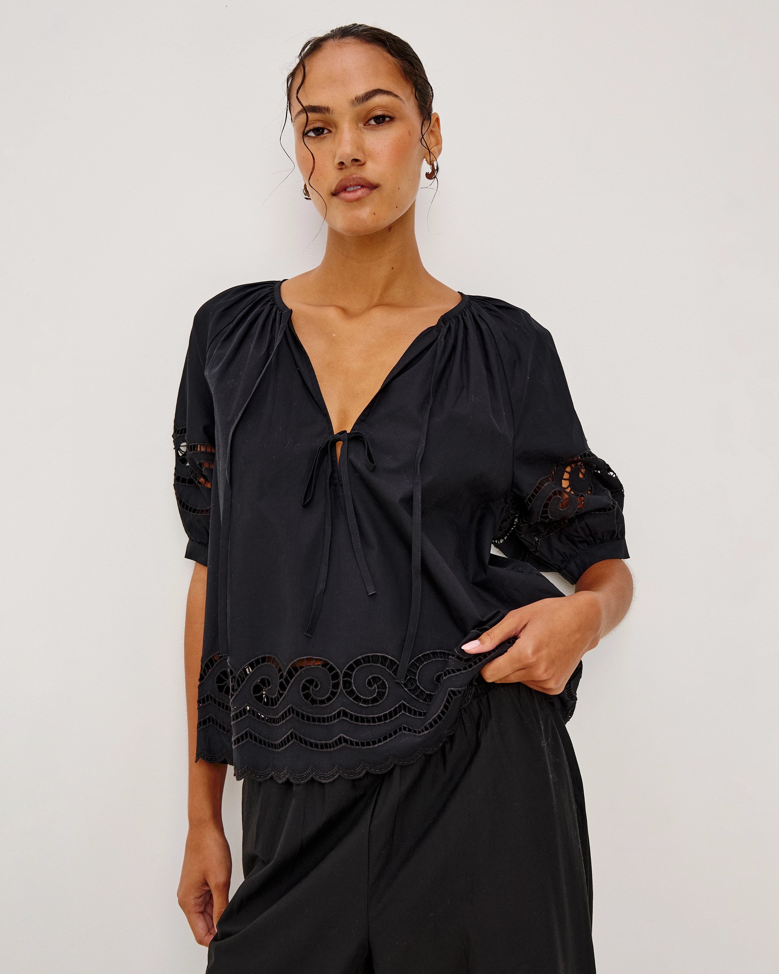 a woman wears a black cotton blouse with embroidery trim details