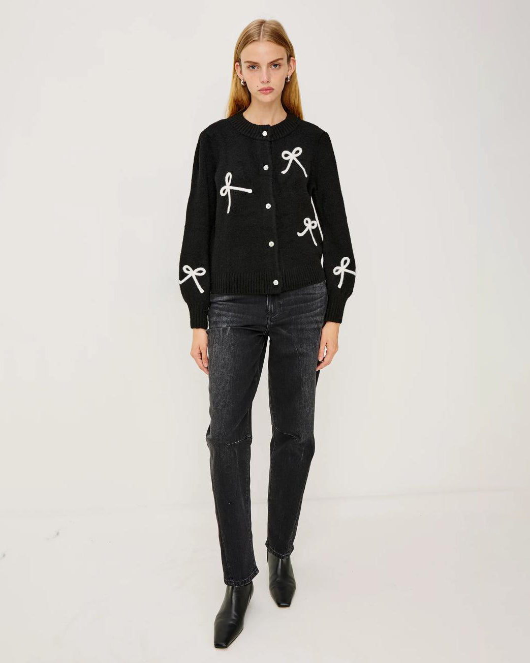 a woman wearing a black button down cardigan with white bow patterns