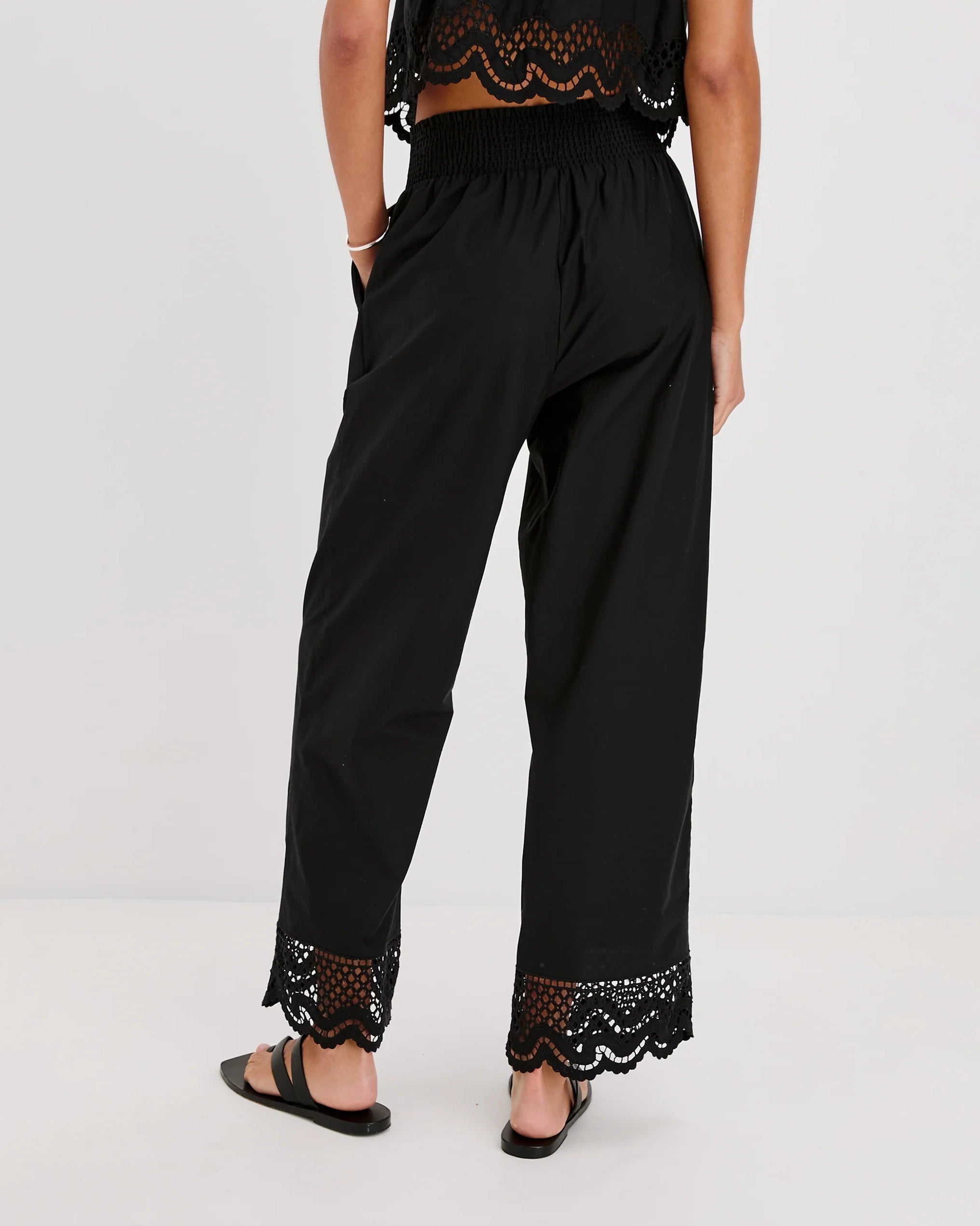 a woman wears black cotton pants with embroidered lacey trim on the hem