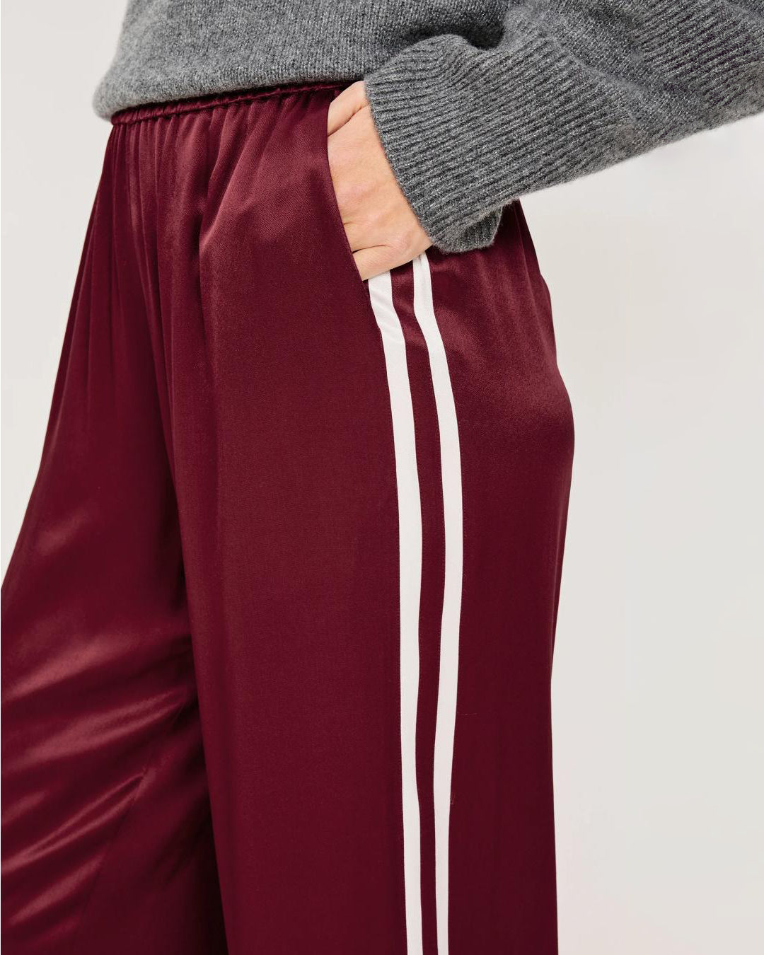 A woman wears maroon satin pants with white stripes
