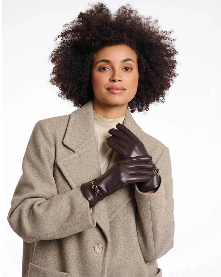 a woman wears a pair of faux leather gloves in dark brown with a gold horsebit detail on the wrist