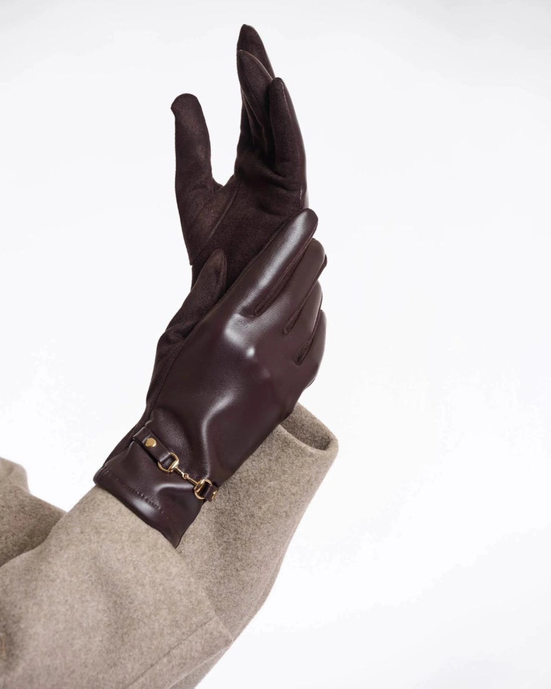 a woman wears a pair of faux leather gloves in dark brown with a gold horsebit detail on the wrist