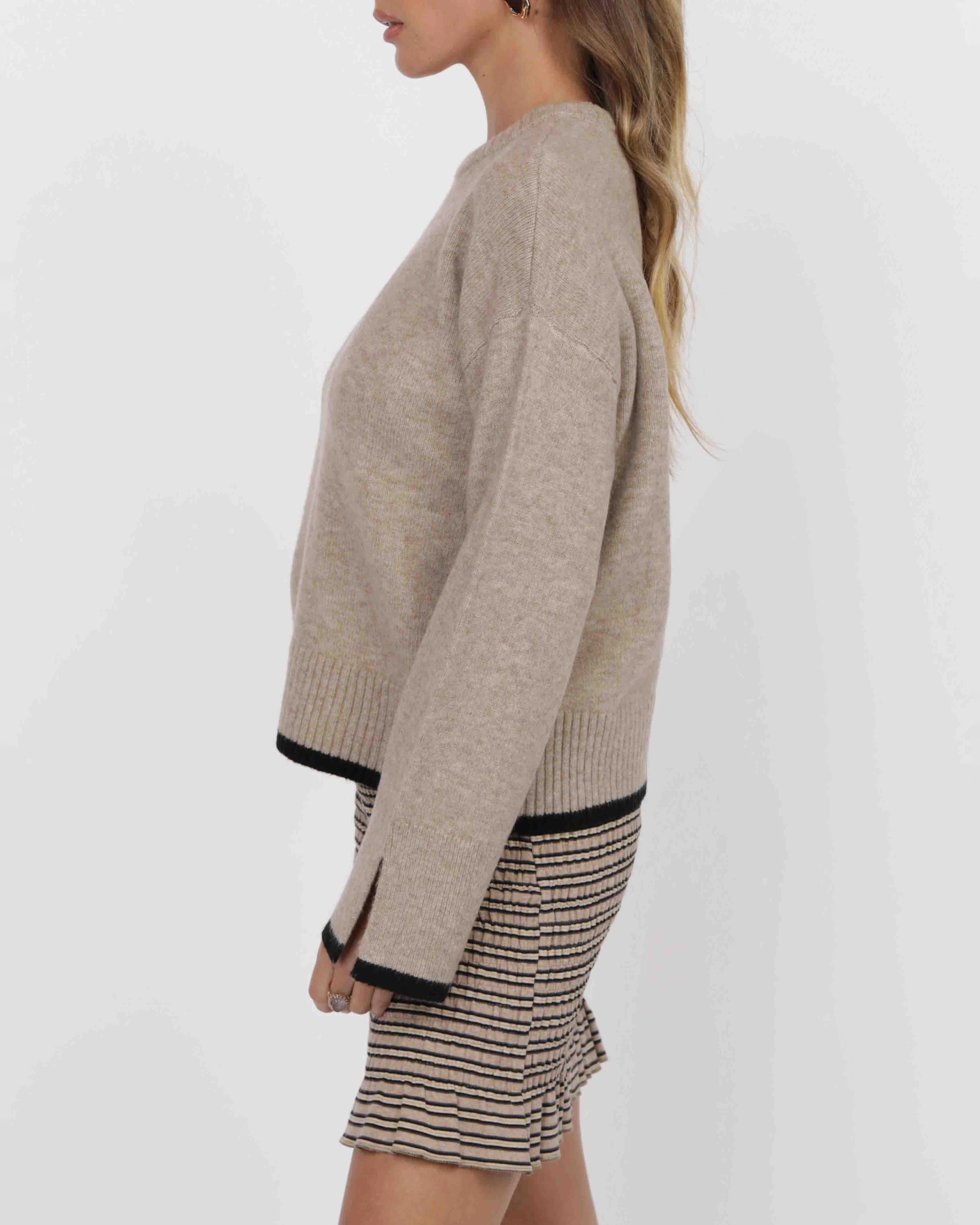 woman wearing a beige knit sweater with black piping