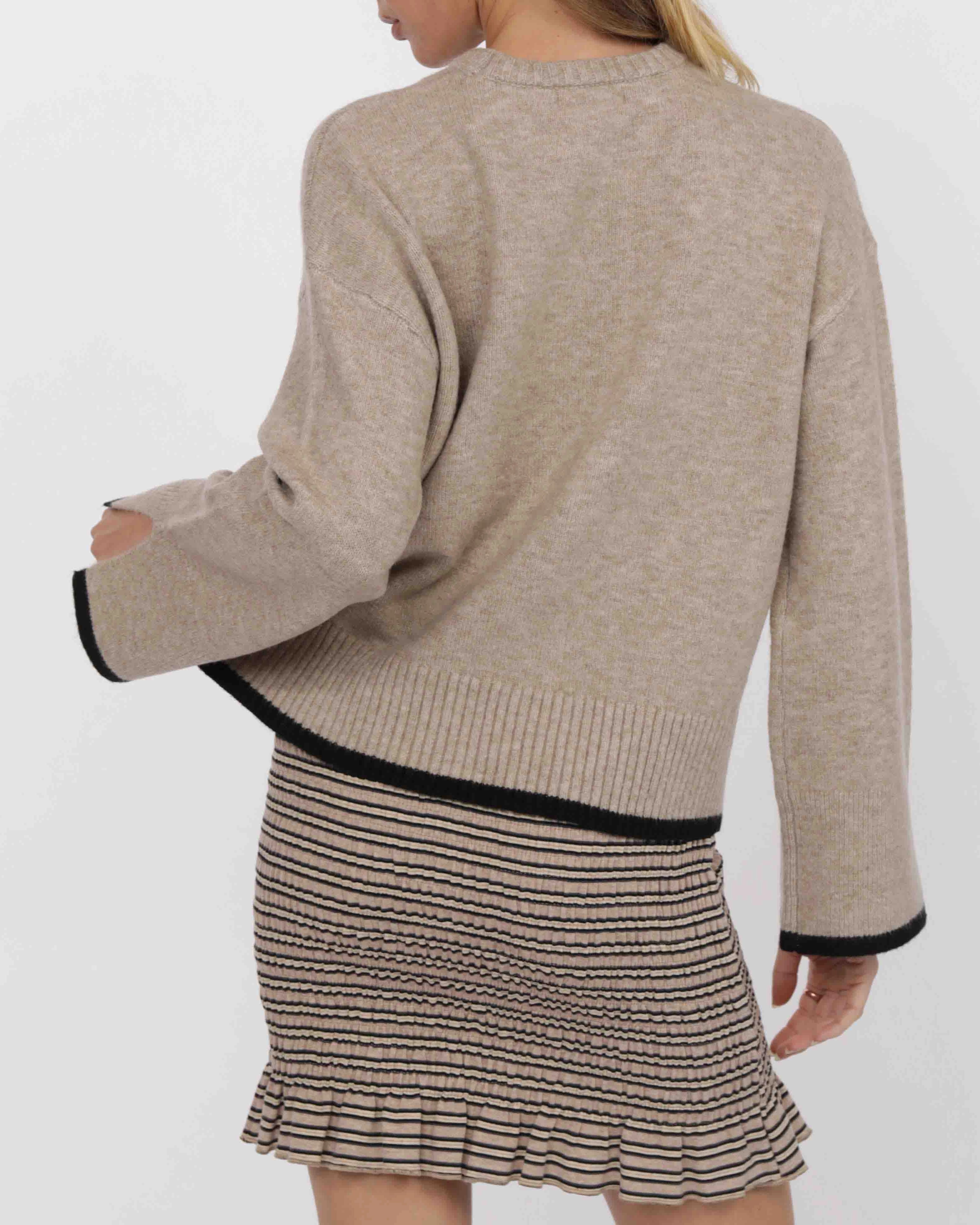 woman wearing a beige knit sweater with black piping