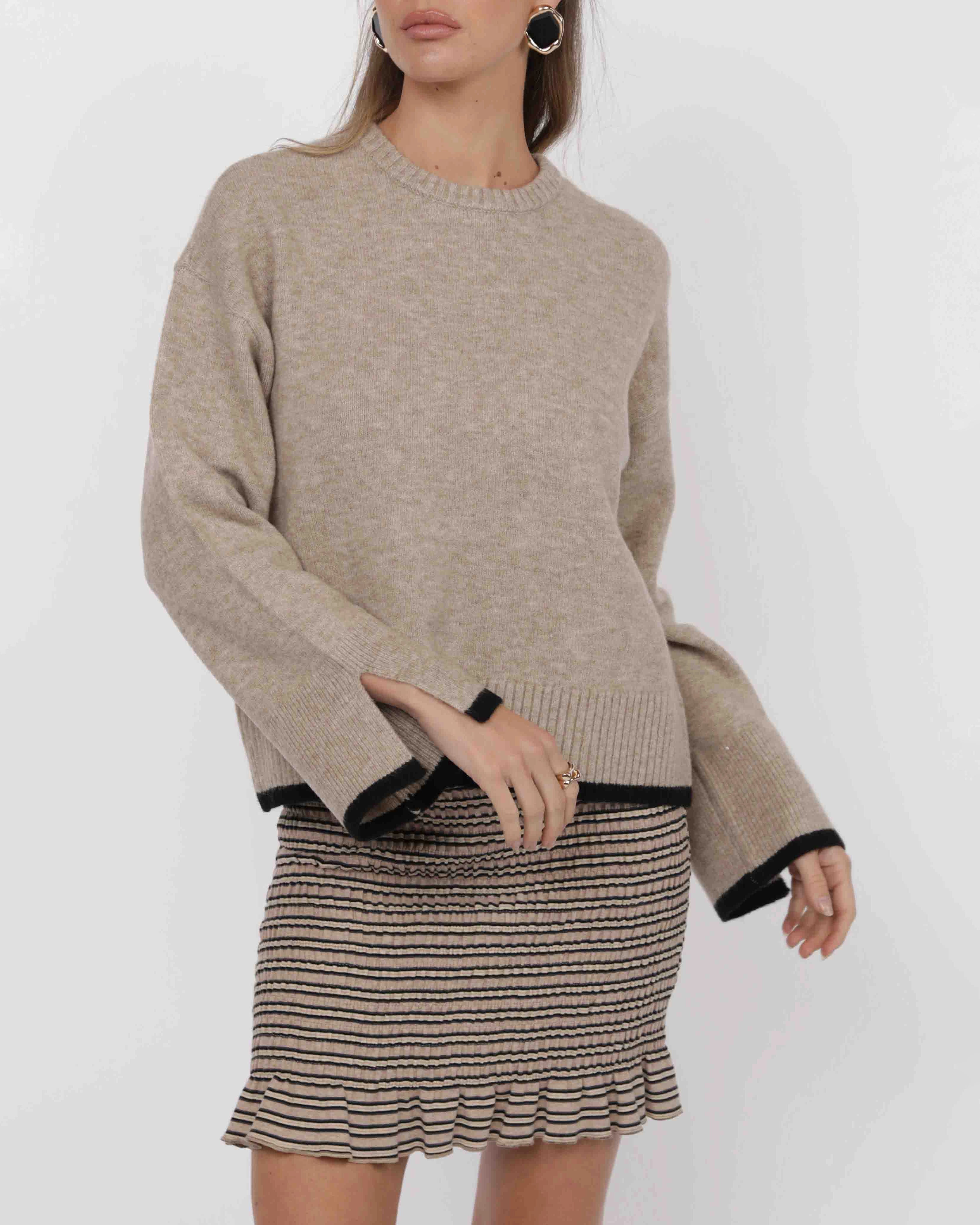 woman wearing a beige knit sweater with black piping