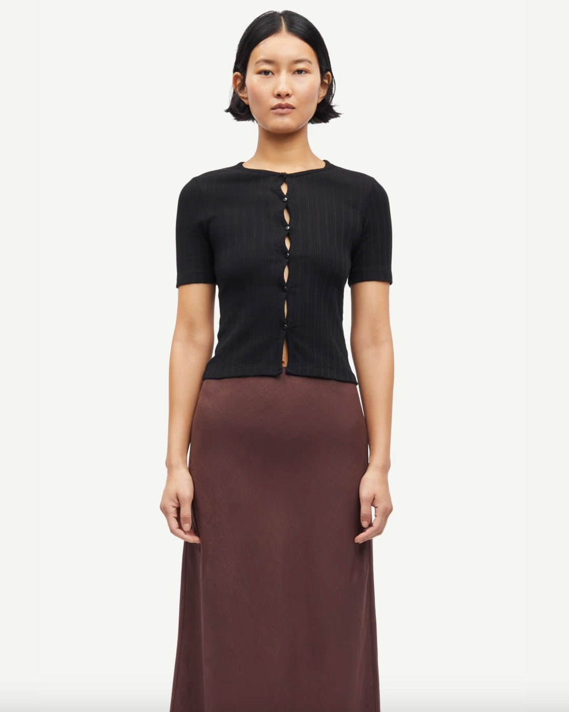 Woman wearing a black short-sleeve button down cardigan top and brown skirt