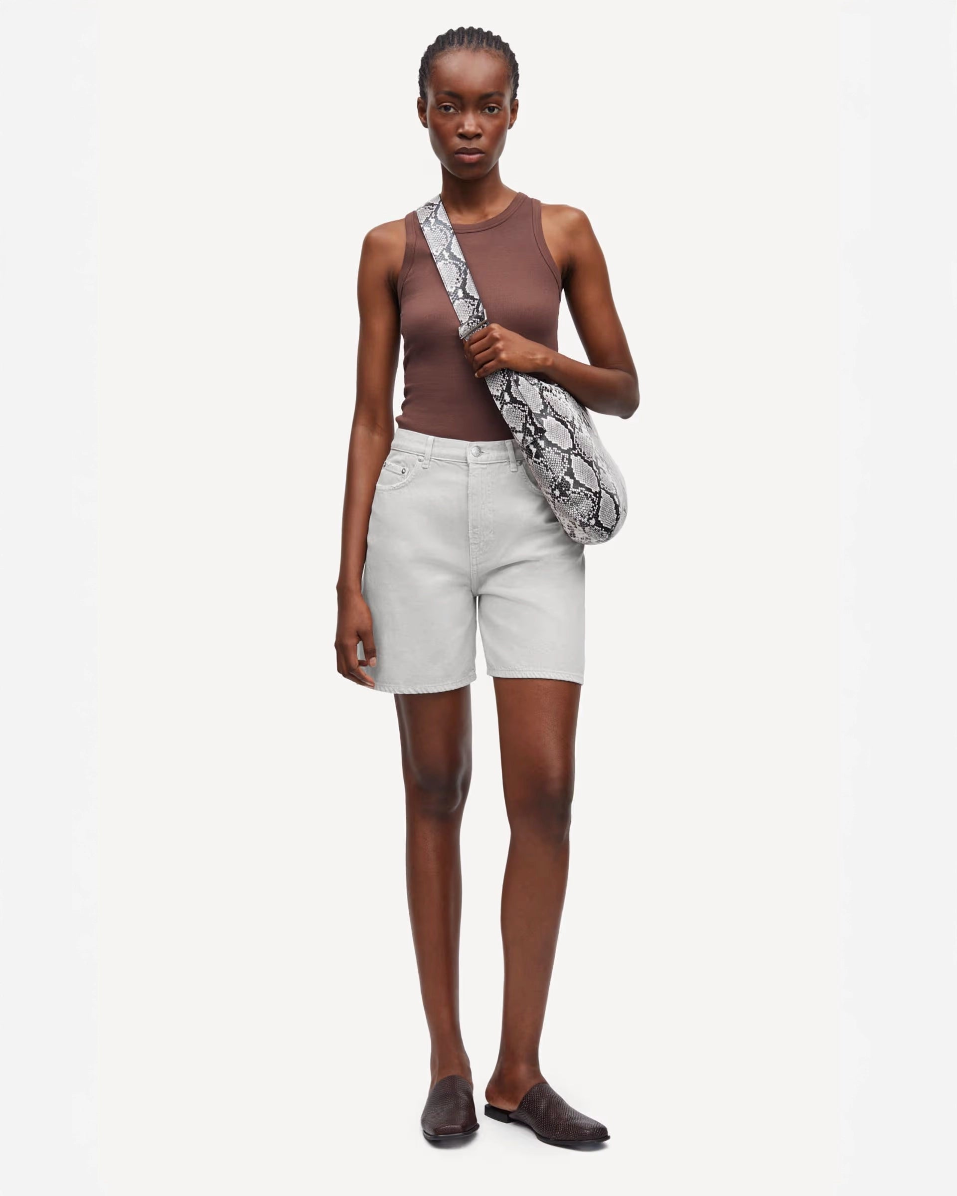 Woman wearing a brown sleeveless top and white shorts, holding a patterned bag
