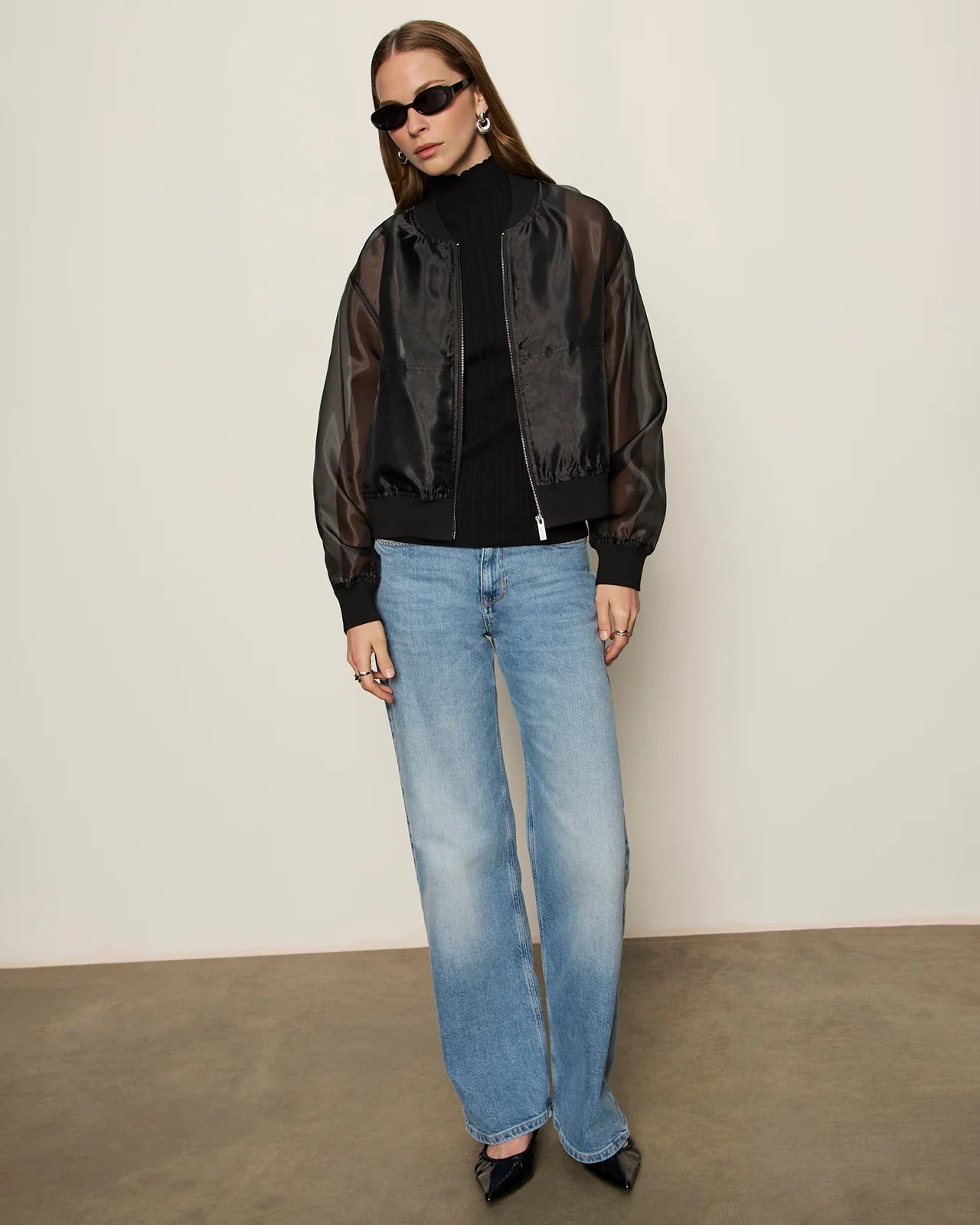woman wearing a black sheer organza jacket over a black turtleneck and blue jeans