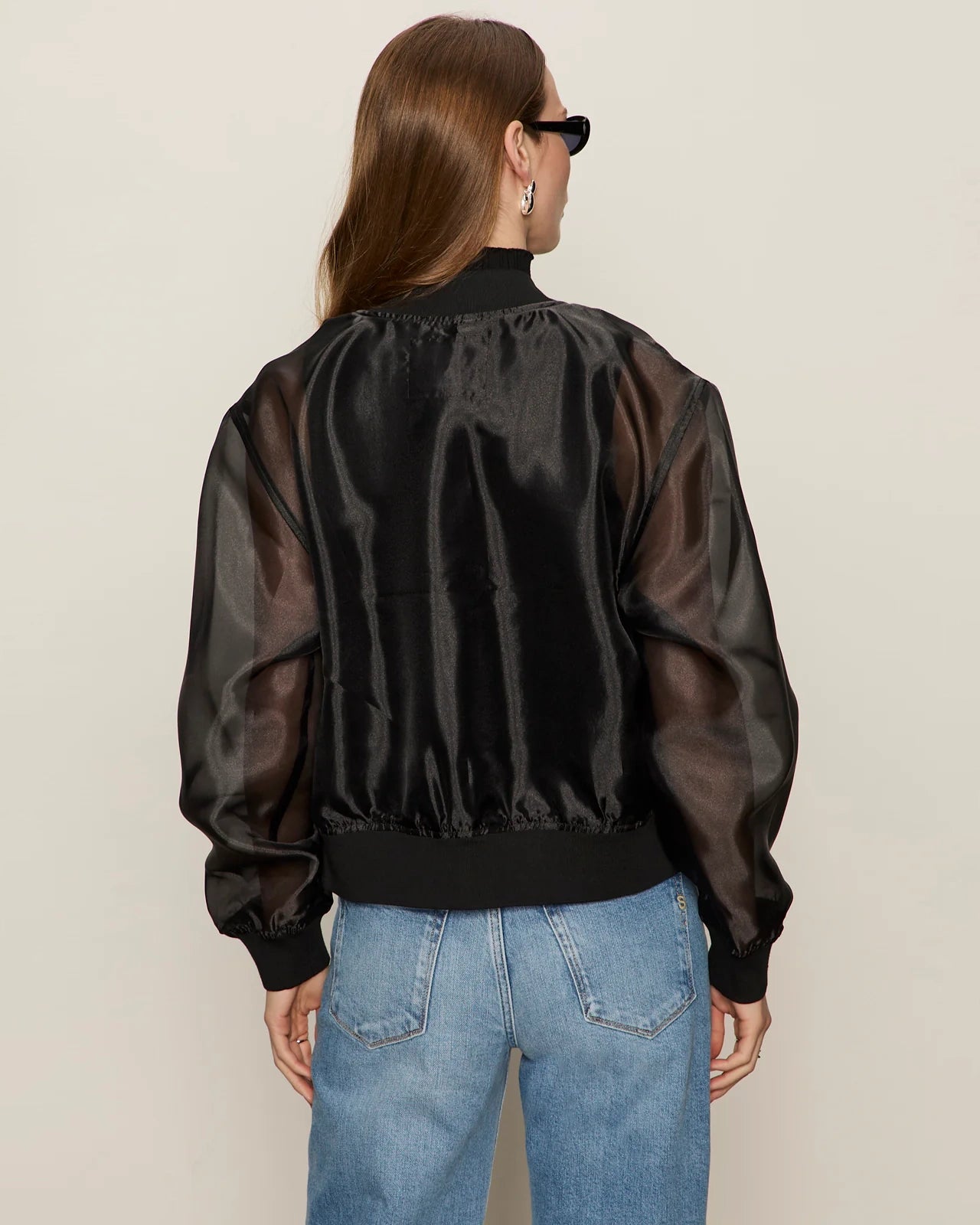 woman wearing a black sheer organza jacket over a black turtleneck and blue jeans